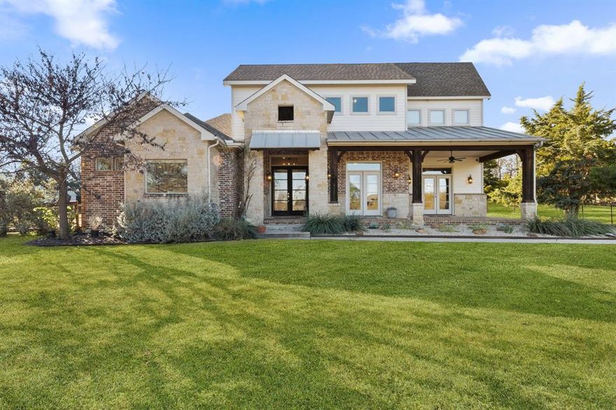 Situated on just under three acres in the heart of Lucas, this custom home offers privacy, functionality, and thoughtful design throughout, tucked away on a quiet cul-de-sac in highly sought-after Lovejoy ISD. A long driveway leads to a striking stone and brick exterior with a welcoming front porch, while inside the layout flows effortlessly for both everyday living and entertaining. Hand-scraped hardwood floors run throughout the main living areas on the first floor, setting a warm and timeless tone. The family room is anchored by a stone wood-burning fireplace and offers expansive views of the pasture and barn, opening to a large covered patio with gas stub for outdoor entertaining. The kitchen provides abundant storage with a five-burner gas cooktop, island seating, and a walk-in pantry with pull-out shelving, while the sunny breakfast room features French doors leading to the oversized covered front porch—an ideal space to unwind. The privately located primary suite overlooks the pasture and includes a large walk-in closet, separate shower, and garden tub. A secondary living area offers flexible use and includes a wet bar with sink and refrigerator, ideal for entertaining or everyday living. Upstairs, a spacious game room is joined by three generously sized bedrooms with walk-in closets, two sharing a bath and one with an ensuite bath. Additional highlights include a side-entry three-car garage with epoxy flooring, a 21x10 workshop with attic storage, 220-amp plug for a welder, and double doors for easy access, all surrounded by open, fenced land with no HOA restrictions.
