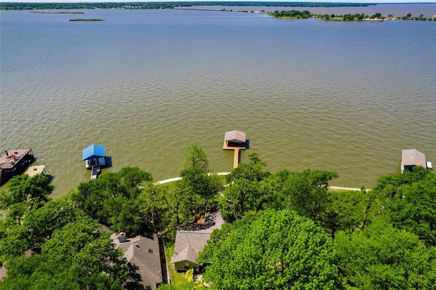 Private retreat on a large, tree-filled lot with expansive open water views.  Designed for lakefront living, this homes features a spacious covered porch and extensive decking, perfect for soaking in the scenery.  A boathouse with personal watercraft lift makes enjoying the water effortless.  Inside, the open-concept living area boasts vaulted ceilings, a fireplace, and a wall of windows, bringing in natural light and panoramic lake views.  Entertaining is seamless with a beverage bar serving both indoor and outdoor spaces.   The dining area overlooks the water, creating a stunning backdrop for every meal.   The private owners suite offers lake views and opens onto its own secluded deck.  Generous-sized bedrooms ensure comfort for family and guests.  With a two car garage and ample parking, this property is ready for unforgettable gatherings.