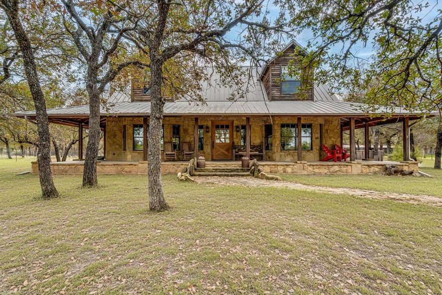 Tucked behind a gated entrance and winding gravel drive, this striking wood-and-stone home sits on 4.8 acres of trees and pasture in the 7R Retreat Community. The metal roof, full wrap-around concrete porch, and inviting front steps framed by native stone give it the feel of a classic Texas lodge from the moment you pull in. Inside you will find 3 generously sized bedrooms and 2.5 bathrooms. The kitchen opens to the living area providing  comfort for daily living.  With an open feel, wood counters, large commercial refrigerator and other built in appliances it is ready for entertaining or comfort. The primary suite is conveniently located downstairs with its ensuite bath that features true relaxation in the oversized tub, a separate shower, double vanities and walk in closet. Downstairs also features a half bath and laundry room with sink. An upstairs area overlooks the main living and can serve as a game room, office, or flexible second living space, with large secondary bedrooms on each side, perfect for guest, family, or just having extra space. This home has soaring ceilings, rich wood finishes, and a massive stone wood-burning fireplace create a warm, lodge-style living area with picture windows that frame the surrounding oaks. 
Outside, your gated entrance opens to a set up to truly enjoy the property. The acreage is cross-fenced with a cleared front pasture, scattered mature trees, chicken coop, open barn, and additional animal shelters—ideal for hobby livestock or simply room to roam. You’ll feel completely tucked away, yet still enjoy all the amenities 7R Ranch is known for, including hiking and riding trails, fishing lakes, stables, fitness and recreation centers, multiple pools, and more. This home and community will truly make you feel like you are on a constant vacation.  Country and small town feel while still within distance to the metroplex for all your other needs. Make this one a place to call home soon!! Its truly one of a kind.