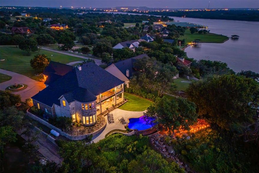 This is your opportunity to own a luxurious waterfront retreat that perfectly blends architectural grandeur with the charm of small town and lakeside living, just 45 minutes from downtown Fort Worth. This 2 story custom masterpiece is a retreat that offers built-in amenities and serenity at every turn. Be welcomed inside to soaring ceilings and an open concept living with panoramic lake views. The show stopping kitchen is a chef’s dream, every detail designed for you to enjoy seamless entertaining and everyday luxury living. Wake up to lake views in the breathtaking primary suite that offers a peaceful escape with a sitting area, spa like bathroom, and two custom closets. Upstairs, you’ll find a media room, a spacious game room with a fully equipped bar, and a large balcony overlooking the sparkling pool and lake beyond. You will never want to leave because this home has it all, gym, salon, wine cellar, and a climate controlled workshop-garage, each thoughtfully designed for function and flair. Adtl. bedrooms provide comfort and privacy for family or guests. Outdoors, the infinity pool appears to spill directly into the lake, surrounded by stone decking, mature trees, and three tiers of entertaining space, including a gazebo, dock, and waterfront access. Whether boating, fishing, or simply lounging poolside at sunset, this is Texas lake living at its finest. Experience the beauty, tranquility, and elevated lifestyle this one of a kind home delivers.