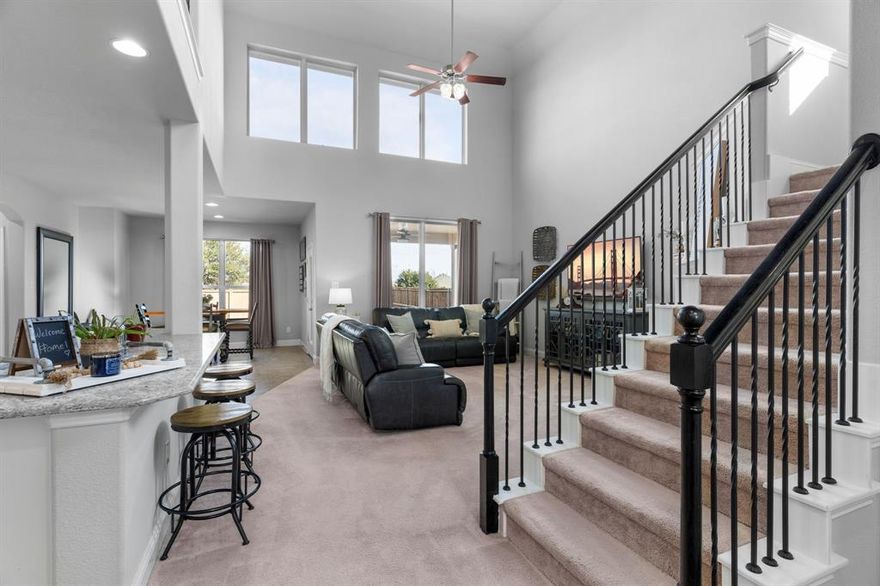 Meticulously maintained two-story brick home with an extended front porch, ideally located in the desirable Trinity Falls community of North McKinney. The striking exterior features black shutters, a herringbone brick detail above the two-car garage, and an elegant front door with frosted glass, wrought iron accents, and keyless entry. Inside, the dramatic front entry impresses with soaring 19-foot ceilings, a chandelier, and a stunning wrought iron staircase leading to a suspended bridge overhead. A private office behind glass-pane French doors offers flexibility as a fourth bedroom. The living room feels both grand and inviting with towering windows, plush carpet, and a gas fireplace with mosaic tile and white mantel. The chef’s kitchen features pristine white cabinetry, soft gray granite countertops, white subway tile backsplash, an oversized island with undermount sink and bar seating, and a large French-door pantry. Whirlpool stainless steel appliances include a built-in oven, gas cooktop, microwave, and dishwasher. The dining area offers backyard views and direct patio access. The first-floor primary suite includes plush carpet, a tray ceiling with fan, and French-door access to the spa-like bath featuring a walnut dual vanity with quartz counters, tiled shower with bench, private water closet, and a spacious walk-in closet with built-ins. The second floor loft could serve as a game room or second office, and the private media room is the perfect space for watching movies or the big game. Two secondary bedrooms and a full bath can also be found upstairs. Entertain guests in the oversized backyard with covered patio, ceiling fan, gas grill stub, wood fence, and open green space. Trinity Falls residents are spoiled with resort-style pools and splashpads, trails, dog and frisbee parks, and an onsite elementary school with quick access to Hwy 75, H-E-B, Buc-ee’s, and McKinney shopping and dining.