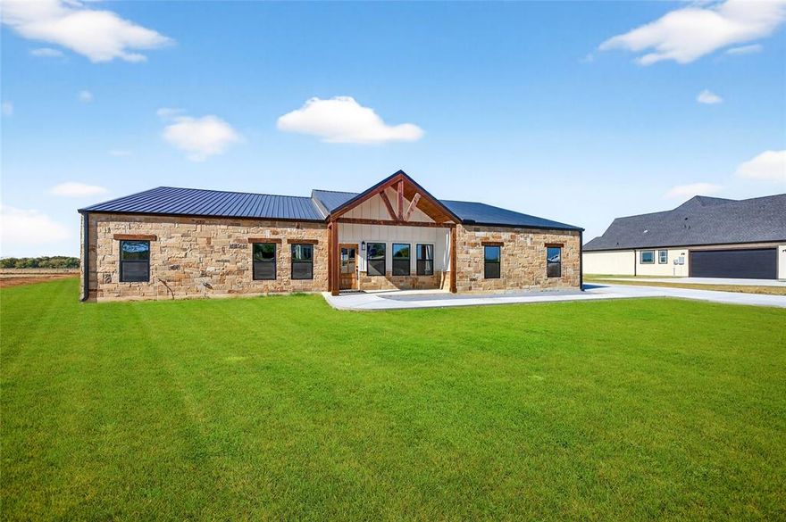 Welcome to Dixie Estates, where Texas charm meets modern design in this stunning custom barndominium set on a full acre in Whitesboro, TX. This thoughtfully designed home offers 4 bedrooms and 3 full bathrooms, with oversized bedrooms that provide plenty of comfort and space for family and guests. The striking stone facade and side-entry garage set the tone for the quality and craftsmanship throughout, with room for all your Texas-sized vehicles, toys, and equipment. Step inside and you’re greeted by soaring ceilings and an open-concept layout that blends the kitchen, dining, and living areas seamlessly. The kitchen showcases high-end custom cabinetry, Quartz counters, and a spacious island, while the living room centers around a decorative fireplace that creates a warm, inviting atmosphere. The private primary suite is a true retreat, featuring a large bedroom, an oversized walk-in shower, dual vanities, and direct access to its own covered porch—perfect for quiet mornings or evenings under the stars. A second covered patio overlooks the expansive backyard, giving you plenty of space to entertain or simply enjoy the peaceful setting. Sod and Landscaping in the works and will be completed prior to closing. Dixie Estates is known for its quality builds, and desirable location just minutes from Lake Texoma, Megastar World Casino, town conveniences while still offering the feel of country living. With high-end finishes, multiple outdoor living spaces, and a functional layout designed for everyday living, this one-of-a-kind barndominium is ready to welcome you home!