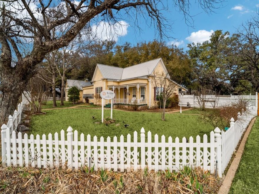 Welcome to The Pomegranate House and Cottage Collection, one of Granbury’s most iconic and distinctive investment opportunities. The Pomegranate House, formerly known as the Ratliff House, was built in 1906 and is an exceptionally well-preserved example of Victorian Eastlake architecture.  Located just 0.7 miles from the Historic Granbury Square and minutes from Lake Granbury, this beautifully preserved historic property blends timeless charm, architectural character, and income potential.  The main home features double primary bedrooms, each with its own ensuite bath, two living areas, a dining room, kitchen, utility-laundry room, and a welcoming covered back porch overlooking a serene courtyard. Surrounding the courtyard are four charming cottages, each thoughtfully designed with a private bedroom and ensuite bath to provide guests with comfort and privacy.  Currently operating as a successful income-producing short-term rental, the property offers six total bedrooms across the main home and cottages. A separate on-site lounge with a fully stocked coffee bar and arcade games enhances the guests' experience. The property also includes a dedicated laundry cottage equipped with multiple washers and dryers, as well as two additional storage and supply rooms to support operations.  The beautifully landscaped grounds are anchored by majestic Live Oak trees estimated to be 300–400 years old, as verified by the Hood County Master Gardeners.  They are living testaments to the property’s enduring legacy.   A peaceful pond with waterfall, inviting outdoor gathering areas, and exceptional curb appeal complete this truly remarkable setting.  Situated on a fully fenced 0.519-acre corner lot, the property is offered fully furnished and fully equipped for a true turnkey opportunity. Endless possibilities await, continued short-term rental use, ideal for family gatherings, boutique hospitality, event venue, office space, or bed and breakfast.