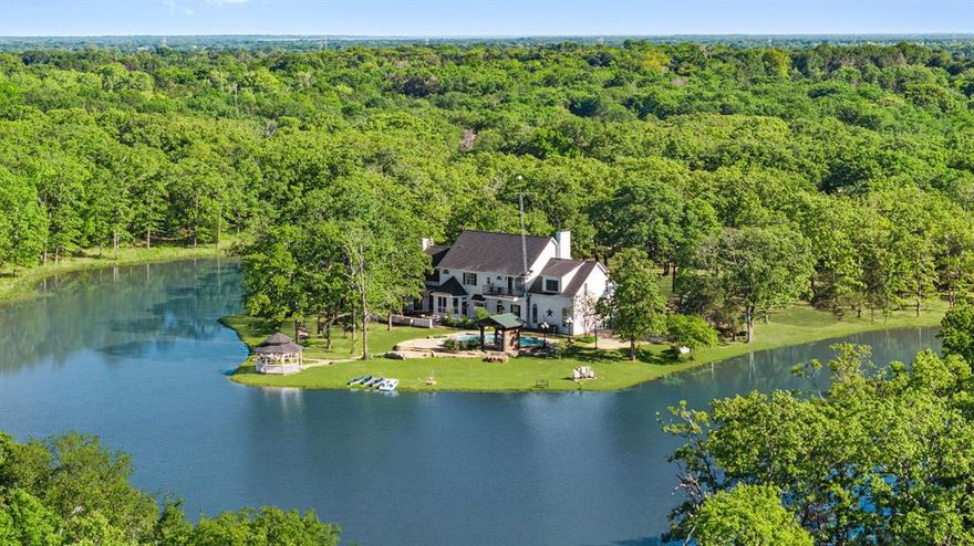 Leave the city behind and immerse yourself in unmatched luxury and seclusion on this extraordinary 50-acre estate. Enter through a gated entrance and follow a lamp-lit, paved driveway that winds through immaculate landscaping and towering trees. At the end of the drive, a stunning 4,780 sq. ft. custom-built manor surrounded by private lake, seamlessly blending classic elegance with cinematic grandeur. Step inside to discover rich hardwood floors, handcrafted finishes, and five stately fireplaces that create warmth and sophistication throughout. The dramatic foyer opens to a formal dining room, a spacious home office or secondary living, and a grand living area complete with a full wet bar—ideal for hosting guests in style. The gourmet kitchen is a chef’s dream, featuring travertine tile, a striking copper backsplash, granite countertops, a large island with a built-in cooktop, and a sunlit breakfast nook.The luxurious owner’s suite offers a peaceful retreat, with its own private sitting area, double-sided fireplace, three walk-in closets, an expansive en-suite bath with Jacuzzi tub and separate shower, and a private balcony with tranquil views. Outside, your personal resort awaits. Relax by the sparkling pool and spa, entertain at the outdoor bar and gazebo, or unwind by the firepit under the stars. Additional features include a 1,025 sq. ft. industrial-grade workshop with a climate-controlled 24x24 space and full bath, a chicken coop, greenhouse, two covered awnings, and miles of private nature trails to explore. A rare offering of timeless sophistication, natural beauty, and total privacy.