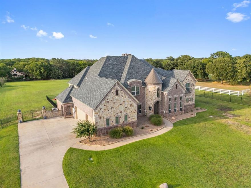 Welcome to Bartonville—where horses and exotic cars share the same scenic roads. Tucked behind a private gate on 2.5 acres, this beautifully renovated home offers elegance and modern country charm. The grand living room boasts 20-ft ceilings with wood beams and a floor-to-ceiling stone fireplace. A gourmet kitchen shines with Calcutta Lux Neolith countertops, luxury appliances including 6-burner gas stove, WOLF double ovens with warming drawer, custom wood cabinetry, large island with secondary sink, and a wine grotto in the butler’s pantry. Featuring 5 oversized bedrooms with en-suites and walk-in closets, including two primary suites on the main floor. Additional highlights include a media room (with surround sound system and electric reclining theater chairs) a game room, central vacuum, private water well, and septic—no water bills or usage limits. The 3-car garage offers EV charging and second laundry hookups. Enjoy quiet and serene evenings on 2 expansive covered patios and an outdoor wood burning fireplace. Backyard is plumbed to build your dream pool. Experience refined Texas living with space, style, and privacy in one of Bartonville’s most coveted settings with amenities close by. Zoned for highly Rates Top 10 ISD - Argyle ISD!