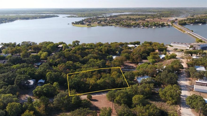 0.35-acre wooded lake view lot in Shamrock Shores community near Lake Brownwood State Park. Features 105ft road frontage on paved Clover Leaf Drive, mature trees providing natural privacy, elevated views of Lake Brownwood. Electric available through Brown County Rural Cooperative, rural water accessible. Flexible county zoning allows residential, manufactured homes, recreational use. Located 12 miles from downtown Brownwood with nearby H-E-B, medical facilities, restaurants. Minutes from 537-acre state park with boat launches, swimming, fishing. Perfect for permanent residence, vacation home, RV retreat, or investment property. Stable market with strong appreciation potential in growing lake tourism area.