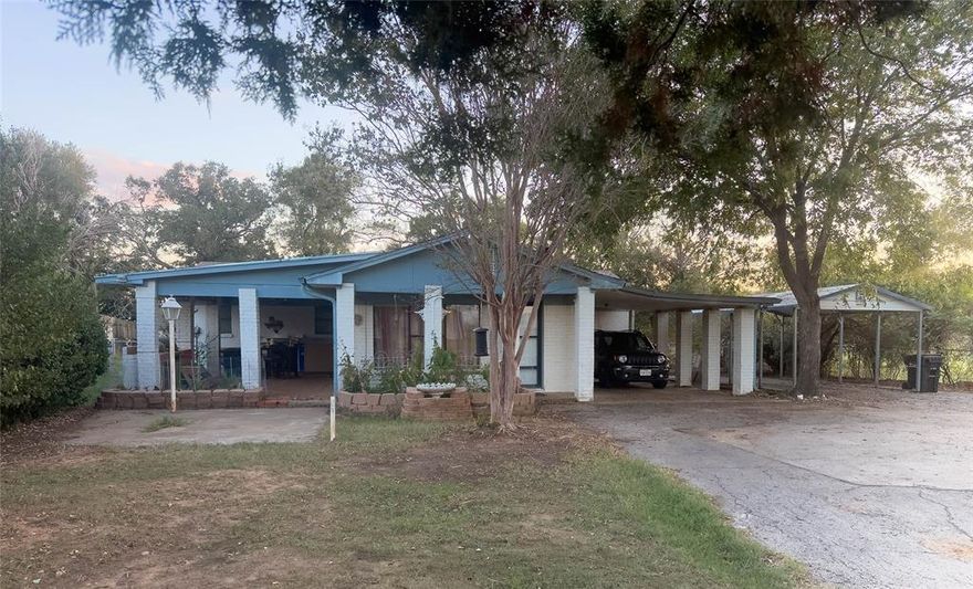 Tucked behind a gated entrance and a driveway lined with blooming crepe myrtles, this welcoming 3-bedroom, 3-bath home offers space, privacy, and a touch of country charm. Set on a .72-acre lot, the property gives you plenty of room to spread out — with both attached and detached carports, a large fenced backyard, storage shed, and dog run. You’ll love the peaceful setting surrounded by shade trees, open sky, and the quiet presence of nearby horses and cows — all just minutes from town. Inside, the home feels warm and comfortable. The oversized living room features a wood-burning fireplace that invites you to relax or gather with friends. The kitchen overlooks the backyard, offering a pleasant view while you cook, and connects to a spacious laundry room with room for a full-size washer, dryer, pantry, and even a drip-dry area. The primary suite includes a large sitting area, built-in shelving, walk-in closet, and walk-in shower — a true retreat. Across the home, the second bedroom with an ensuite bath is perfect for guests, extended family, or multi-generational living.  Step outside to your own outdoor haven: a covered patio with a built-in grill, ideal for weekend cookouts or peaceful evenings under the trees. This property blends comfort, functionality, and country serenity — the perfect place to slow down, stretch out, and enjoy the simple things in life.
