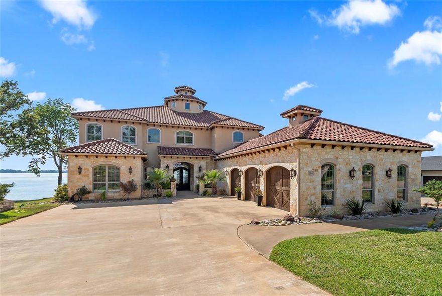 This stunning 2018 home, inspired by the timeless elegance of a Tuscan villa nestled in the foothills of Italy, offers 5,570 sq ft of refined waterfront living on a half-acre lot with 94 feet of open water frontage in the prestigious Pinnacle Golf Club at Cedar Creek Lake. Located in one of the most sought-after areas of the community, it's within walking distance to the clubhouse, restaurant, pool, and fitness center—and perfectly positioned next to the annual July 4 Pinnacle fireworks show for front-row lakeside views. Designed for both luxury and livability, the home features 5 bedrooms, 6 baths, 3 living areas, an office, exercise room, and a 3-car garage. A grand foyer welcomes you with a winding staircase, inlaid tile, chandelier, and sweeping lake views that instantly transport you to a Mediterranean retreat. The main living area is anchored by a stone fireplace and wet bar, flowing into a dining space with butler’s pantry into a second spacious living area. The gourmet kitchen boasts a Thermador 6-burner gas range with pot filler framed in stone, Thermador fridge, custom cabinetry, and walk-in pantry. The waterside primary suite features soaring ceilings, plantation shutters, dual vanities, jetted soaking tub, walk-in shower, and two spacious closets. A private office and two full guest baths, including one with outdoor access, complete the main floor. Upstairs offers four bedrooms—two with en suite baths—and a private guest suite with its own living area. A bonus room with wet bar and balcony, plus an exercise room and full bath, create more space to unwind. Outdoor living includes a firepit, full-length balcony with composite decking, and kitchen with griddle and sink. The boathouse offers a boat slip, dual PWC lifts, and a covered seating area. Ownership includes social membership with clubhouse dining, pool, fitness center, tennis and pickleball; golf memberships available separately