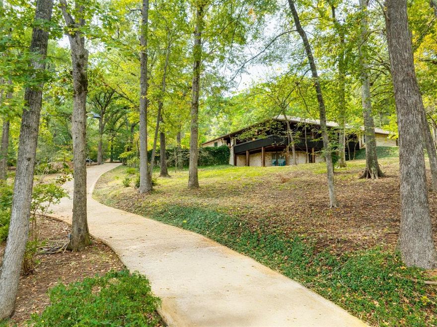Hidden among towering trees in historic Palestine, this custom-built Mediterranean-style home is a one-of-a-kind sanctuaryblending architectural artistry with the beauty of nature. Located on a 4.7-acre hill beside Davey Dogwood Park, a windingconcrete drive leads you through lush foliage to the residence, where a charming fountain patio framed by azaleas anddogwoods sets a tranquil tone. The Saltillo-tiled front porch invites you to linger before stepping onto the elevatedwraparound deck, where you are embraced by the canopy of trees and endless views of the surrounding landscape. Inside,double entry doors open to an impressive hexagonal living room anchored by a wide arched brick fireplace, while a stunningstained & beamed wood ceiling soars above. Expansive picture windows throughout capture the natural beauty outside,bringing light and tranquility into nearly every room. The dining room, featuring a painted wood ceiling, opens to thedeck—perfect for alfresco dining or quiet moments overlooking the trees. At the heart of the home, a sunken octagonalkitchen surrounded by a Saltillo tile hall & walls of glass glows with tree shaded light. Three sets of intricately carved doublewood doors add architectural distinction, while chefs will appreciate the Jenn-Air appliances and casual breakfast nookoverlooking the private backyard. The primary suite offers a retreat with warm wood floors and a spa-inspired bath featuring asoaking tub, multi-head shower, dual sinks, and generous closets. A spacious family room showcases whitewashed woodwalls, vaulted beamed ceilings, a bar with sink, and to the guest wing with an ensuite bedroom, an additional bedroom or office,and a full guest bath. Outdoors, enjoy a patio overlooking a large back yard as well as fruit trees & raised garden beds withina fenced garden area. For those who cherish privacy, nature, and distinctive design, this exceptional home is an inspiringhaven unlike any other.