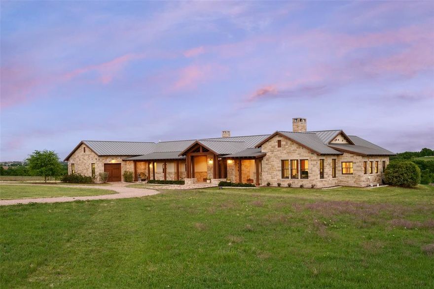 Set on 12.5 picturesque acres in Tarrant County within a private gated community, this extraordinary custom home, built by Dan Thomas Homes, masterfully designed by architect Duke Garwood, offers an unparalleled blend of thoughtful craftsmanship, and serene country living, all just a short drive from Fort Worth. Encompassing 4,329 square feet, this beautifully designed ranch-style home features 5 bedrooms and 4.5 bathrooms, with an open-concept layout that effortlessly accommodates both everyday living and upscale entertaining. The primary suite, office, and great room all showcase dramatic custom Trestlewood reclaimed beams. A stunning handcrafted stone fireplace serves as a focal point in the Great Room, complemented by a second stone fireplace in the kitchen or den, enhancing the home’s warm, inviting atmosphere. The chef’s kitchen is outfitted with premium Monogram appliances, a custom-designed walnut butcher-block island, and ample space for gathering. Throughout the home, Kolbe French doors and windows flood the interiors with natural light while sweeping views of the surrounding acreage and providing direct access to expansive cedar-covered porches. The private primary suite is thoughtfully positioned away from the secondary bedrooms, offering a tranquil retreat with space and privacy. Additional interior highlights include a functional breezeway, a well-appointed laundry area, a built-in concrete storm shelter, and an array of custom finishes and design details that elevate the home. The exterior showcases a custom combination of stone and stucco, perfectly complementing the natural landscape. Beyond the main residence, the property features a well-equipped Morton barn complete with four stalls and a run turnout. A component-built horse barn can easily be converted into a man cave, workshop, car storage, or endless other possibilities to suit your lifestyle. This one-of-a-kind property offers refined country living with convenient access to city amenities.