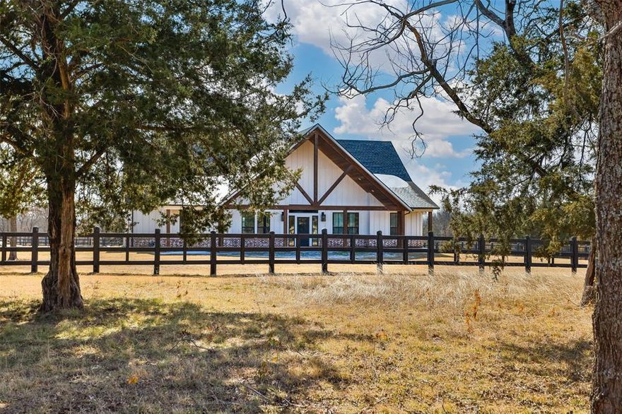 Nestled on 14 private, picturesque acres just minutes from Lake Ray Roberts, this gorgeous custom-built estate offers the perfect blend of luxury, privacy, and country charm. Enter through the piped entrance and follow the winding drive through mature trees as the home reveals itself..peaceful, private, and absolutely stunning! Inside, the home showcases a spacious open concept floor plan designed for both everyday living and entertaining. The gourmet kitchen is a showstopper, featuring marble countertops, a large island, custom cabinetry, gas range, wine cooler, and a Butler’s pantry, all thoughtfully designed with timeless finishes. The living room is warm and inviting with handsome wood beams, a beautiful fireplace, and expansive sliding glass doors that frame serene views and lead to the covered back patio and outdoor kitchen..ideal for relaxing or hosting gatherings. The private primary en suite offers a peaceful retreat, while two guest bedrooms with a dual bath arrangement provide comfort and convenience on the main level. Upstairs, you’ll find an additional bedroom and full bath. Throughout the home, custom wood accents, detailed ceiling treatments, brick feature walls, and builtin elements add character and craftsmanship. A dedicated office or flex space provides versatility for work or hobbies. Outside, the property continues to impress with a scenic fishing pond complete with a walk out dock, perfect for quiet mornings or evening sunsets. A 700 square foot guest house offers two bedrooms and one bath, ideal for guests, multigenerational living, or rental potential. Additional features include a 30x50 slab ready for a future workshop, chicken coop, garden area, loafing shed, split rail fencing, and wide-open spaces to enjoy the land. This one of a kind property offers refined country living with room to grow, all in an exceptional location near the lake. A rare opportunity to own a private retreat with luxury, land, and lifestyle all in one.