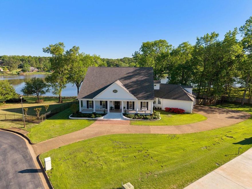 Welcome home to lakefront living at its finest in Bullard! Located in the sought-after Pecan Valley Ranch subdivision, this custom home overlooks the peaceful waters of Lake Lou Ella, a private neighborhood lake known for great bass fishing and quiet recreation, all just minutes from Tyler’s shopping, dining, and medical at The Village at Cumberland Park. From the moment you arrive you will be drawn to the home's timeless Southern Charm with its wide verandas, gas lanterns, and porch swings, all setting the tone for relaxed East Texas living, where lake breezes and towering trees invite you to slow down. Inside, a grand foyer with a curved staircase is flanked by a formal dining room and a private guest suite with ensuite bath. The spacious living room with a floor to ceiling stone fireplace opens to a chef’s kitchen featuring custom cabinetry, gas cooktop, double ovens, large island with bar seating, butler’s pantry, and a dedicated coffee station. A built in workspace sits just off the kitchen, while the breakfast nook with window seat captures beautiful panoramic lake views. The primary suite offers a true retreat with a sitting area, two sided fireplace, patio access, and serene water views. The ensuite bath includes a jetted tub, stained-glass windows, walk-in shower, dual vanities, and a large closet with direct access to the utility room. Upstairs features a game and media room with custom booth seating, movie screen, and half bath, along with two bedrooms sharing a Jack and Jill bath. A separate bonus room above the garage provides flexible space for a gym, studio, or playroom. Out back, a covered patio overlooks the lake, perfect for relaxing or entertaining. Enjoy fishing, kayaking, and paddleboarding right from your backyard. Rare waterfront living with space, function, and convenience, homes on Lake Lou Ella don’t come up often. Call today for your private showing!