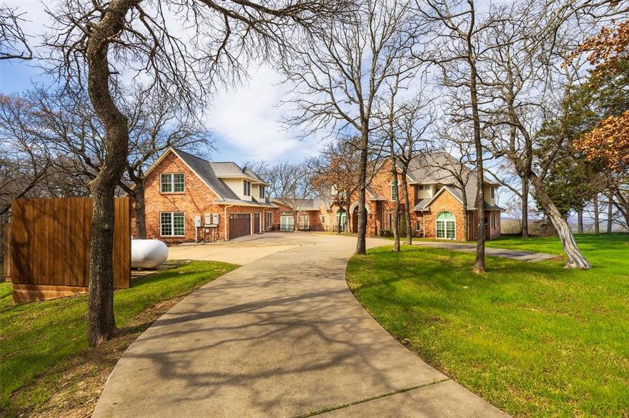 Welcome to this stunning Lake Lewisville lakefront estate with sweeping water views. The recently updated main home features new flooring, fixtures, and renovated kitchen and baths. The grand living area showcases a dramatic staircase, stone fireplace, and expansive lake views. A stately study offers hardwood floors, built-ins, rounded windows, and a hidden storm shelter. The gourmet kitchen features hardwood ceiling accents, ample storage, an island with prep sink, industrial built-in refrigerator, and Viking hood. The breakfast nook and patio provide beautiful lake views. The oversized primary suite includes bay windows overlooking the water, sitting area space, and a spa-like bath with dual vanities, garden tub, separate shower, and two walk-in closets. Upstairs includes a game room with bay windows and wet bar, plus additional bedrooms with Jack-and-Jill bath. A separate apartment above the garage includes a kitchen, living area, bedroom, and full bath. Enjoy outdoor living with multi-level patios, stone pathways to the water, and wooded privacy. Additional features include oversized garage, geothermal HVAC, 3 water heaters, 5 heat pumps, and propane generator.