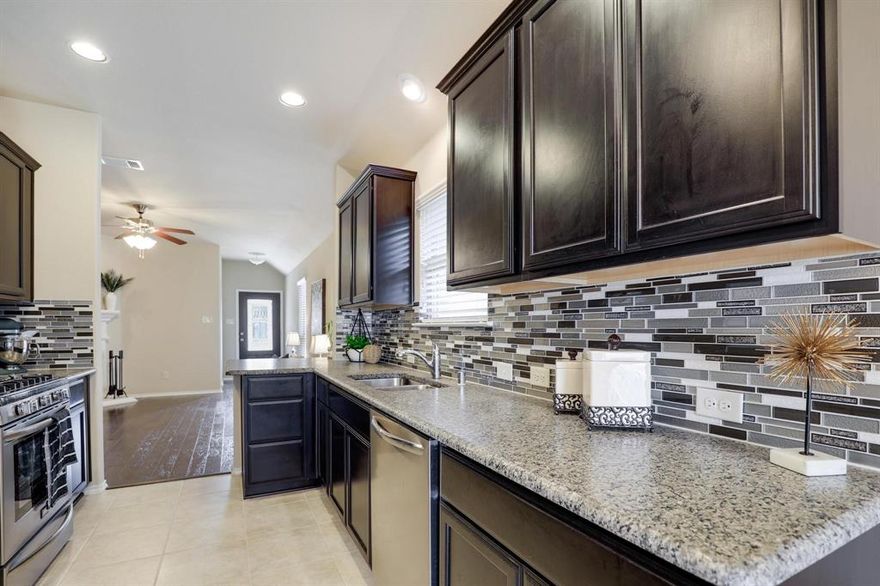 Beautiful single-story brick home accented with stone details, ideally located in the Fossil Creek at Westridge community in McKinney. A landscaped front yard welcomes you to a covered brick porch and a wood front door with frosted glass detailing, complete with a Ring doorbell camera. Upon entry, engineered wood floors extend throughout the home, complemented by abundant natural light and a vaulted 9-foot ceiling. The spacious living room features a ceramic wood-burning fireplace with gas starter, creating a cozy focal point, and includes a mounted TV. The pristine galley-style kitchen offers tile flooring, dark walnut cabinets with crown molding, leathered granite countertops, mosaic tile backsplash, an undermount dual sink, bar-height peninsula seating, Frigidaire stainless steel appliances, and an oversized walk-in pantry. The private primary suite features wood floors, serene backyard views from two windows, a vaulted ceiling with fan, and French doors to the en suite bathroom. The primary bath includes a walnut dual vanity with upgraded granite countertops and undermount sinks, updated walnut-framed mirrors, elegant glass light fixtures, a soaking tub, separate tiled shower, private water closet, and a generous walk-in closet with built-in shelving. Two secondary bedrooms feature wood floors, vaulted ceilings with fans, and ample closet space. A full bath offers a walnut vanity with upgraded granite countertop, updated mirror, and tub-shower combo. Additional amenities include upgraded arched interior doors, security system wiring, Honeywell thermostat, upgraded remote sprinkler system, transferable home warranty through May 2027, a 2-car garage, and recent updates including a 2023 roof, fresh paint, mirrors in both bathrooms, and patio tile. Enjoy the covered back porch with new tile flooring and ceiling fan, a spacious fenced yard, and access to the community pool just a one-minute walk away. Zoned for Prosper ISD.