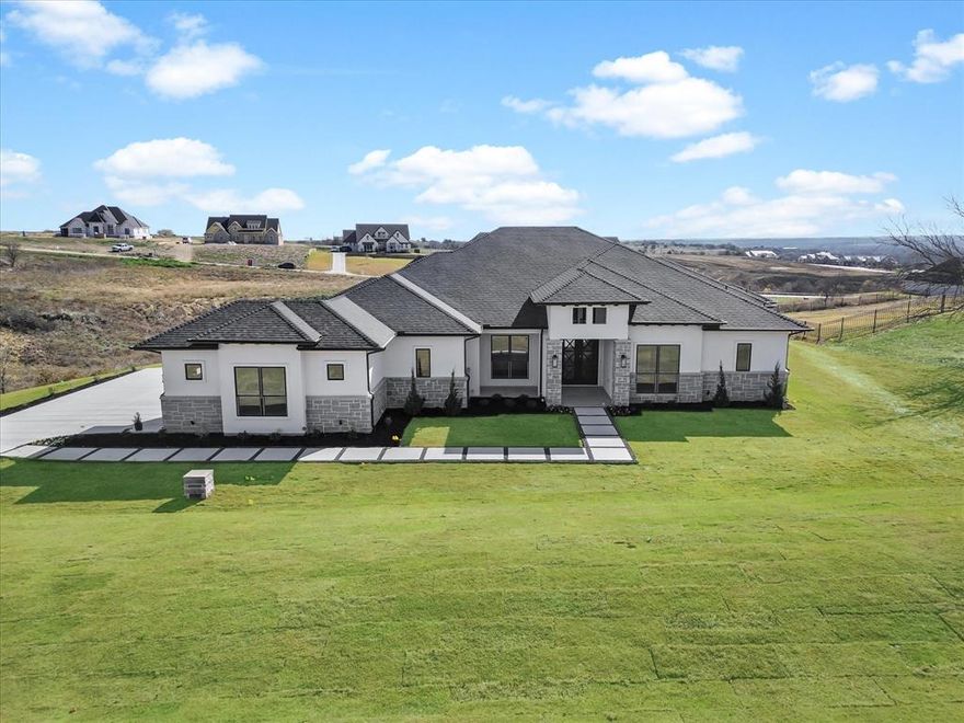 Welcome to this stunning custom home tucked away on a quiet cul-de-sac in the prestigious Bella Crossing community. Perfectly positioned on a sprawling elevated lot, the home offers picturesque hilltop views that stretch for miles and a rare combination of privacy, luxury, and thoughtful design. Inside, an expansive open floor plan showcases soaring 15-foot ceilings with exposed wood beams and abundant natural light. The grand family room, anchored by a sleek electric fireplace, flows seamlessly into the chef’s kitchen ideal for entertaining and everyday living. The kitchen features a premium Thermador appliance package including a gas range cooktop and double ovens, custom cabinetry, a spacious walk-in pantry, and an oversized quartz island with dramatic double waterfalls.

Designed with comfort and privacy in mind, each secondary bedroom offers its own en-suite bathroom and walk-in closet. The primary suite is a true retreat with a spa-inspired bath featuring dual vanities, a soaking tub, a walk-in shower, and a large custom closet with built-ins. A private study with French doors and beamed ceilings creates the perfect work-from-home space, while the spacious utility room includes a sink and ample storage. The home has been lightly lived in and meticulously maintained. The exterior blends stucco, stone, and brick with a striking iron front door for timeless curb appeal. An oversized three-car garage offers extended length, easily accommodating larger vehicles or trucks. Enjoy outdoor living on the covered patio while taking in the sweeping views. Conveniently located with quick access to Chisholm Trail Parkway and Interstate 20, this location also benefits from the exciting future growth surrounding the upcoming Bluejack Ranch 18-hole championship golf course, and resort-style facilities designed by Tiger Woods. This home is a dream!