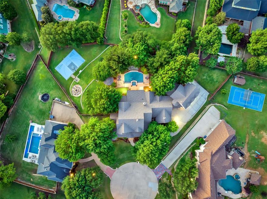 Poised on a quiet cul-de-sac in one of the most sought-after gated communities, this GG Cain custom-built showpiece redefines luxury living. This rare gem showcases a 7-car garage, offering unparalleled space for car collectors or recreational enthusiasts. The terraced backyard becomes your daily retreat. Designed for both relaxation and recreation featuring a pool and spa, gazebo, putting green, basketball court, and firepit lounge, all perfectly positioned to capture stunning panoramic sunsets. The home exudes a refined Modern Farmhouse aesthetic with a wraparound front porch and sophisticated luxury appointments throughout. The gourmet kitchen is a culinary dream, boasting a Thermador gas range, Miele built-in coffee system, pot filler, marble countertops and backsplash, apron-front farmhouse sink, walk-in pantry, and additional chef’s pantry. An entertainer’s paradise, the den features a show-stopping bar with waterfall island, sink, wine and beverage refrigeration, and ice maker—perfectly flowing into the living room. Sliding glass doors reveal a fully-equipped outdoor living area with a stone fireplace, Lynx professional-grade kitchen, and four ceiling-mounted Infratech heaters for year-round enjoyment. The primary ensuite is a private haven wrapped in marble with a romantic clawfoot soaking tub, frameless glass shower with rain head, dual vanities, and a designer dressing room complete with an island and glass-front display cabinetry worthy of a boutique. A spiral staircase leads to a sprawling man cave with its own full kitchen, living room with fireplace, full bath, and separate exterior access. The thoughtfully designed floor plan also includes a formal dining room, private study, main-level guest suite with ensuite bath, and utility and mud rooms. Upstairs features a media room with theater seating and wet bar, three additional bedrooms (one with whimsical built-in bunk beds and another with a private sauna), plus two walk-out attic storage spaces.