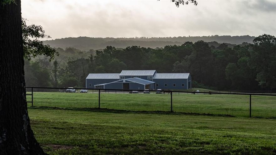 Nestled on a quiet county road just 10± minutes from Tyler, Hidden Oaks Ranch offers 50±AC of peaceful seclusion, lush rolling pastures, and premier equestrian amenities—all within reach of town. Situated on the property’s highest point, the ranch-style home offers 5 bedrooms, 3.5 baths, and sweeping views of the surrounding paddocks and pastures through oversized windows and French doors. The equestrian facilities feature a renovated 24-stall barn with a 1,920± SF second-story addition, ideal for building out guest or ranch staff quarters. The barn offers two tack rooms, a stone wash rack, grooming bays, laundry room, office spaces, and a bathroom, the setup is designed for both private use or a professional training program. A shaded path winds to a lit 150x300’ outdoor arena, perfect for riding or hosting clinics. There are 11 pipe-and-no-climb fenced turnouts that provide safe, sandy footing—perfect for turnout, exercise, and grazing. A scenic pond and approximately 80’ of soft elevation change add natural beauty and character to the land. Located in Whitehouse ISD and outside city limits, this turn-key ranch offers privacy and potential for those seeking a working horse property, weekend retreat, or long-term homestead in the heart of East Texas.