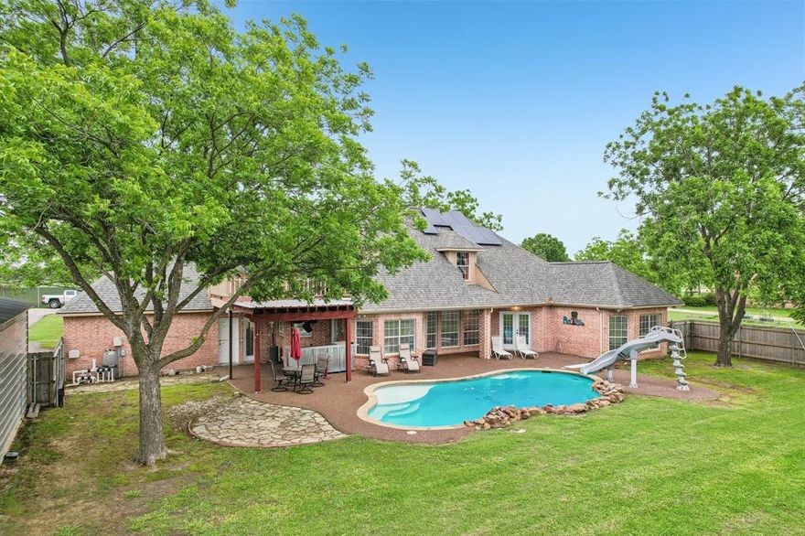 1 acre in Ennis, TX featuring a 5 bedroom, 3.5 bath home with 3,226 sq ft built in 2000, a 24x40 insulated workshop with electricity, 2 car carport, and 3 car garage. Recently upgraded concrete driveway provides additional parking space and convenience. The backyard offers a resort style pool with waterfall and water slide, along with recently added rubber cap surfacing for durability and comfort around the pool and patio, all surrounded by mature pecan trees. Fully paid off solar panels provide long term energy savings. This beautifully maintained home offers a functional open floor plan designed for everyday living and entertaining. A welcoming entry with upgraded rubber cap flooring creates a clean, durable, and modern first impression. As you enter, you find a dedicated office space, an open living room with a brick fireplace, abundant natural light, and large windows overlooking the backyard. The kitchen includes granite countertops and ample cabinetry, with a dining area that flows seamlessly for gatherings. The laundry room includes a sink and storage cabinets. The first floor features a split primary suite for added privacy. One secondary bedroom connects directly to the primary closet, offering flexibility for a nursery, gym, or flex space. A full bathroom serves the secondary bedrooms, along with a half bath with convenient outdoor access to the pool. Upstairs includes a media room with balcony access, an additional bedroom or game room, and a full bathroom, creating a private second level retreat. Major updates include recently completed foundation repair with transferable documentation, two water heaters replaced within the last two years, HVAC system serviced twice yearly across three AC units, and septic system serviced every four months with the seller covering an additional year, and freshly repainted. Located in a quiet neighborhood with a dead end feel and easy access to Highway 287. Everything a Texas home has to offer on a full acre in Ennis.