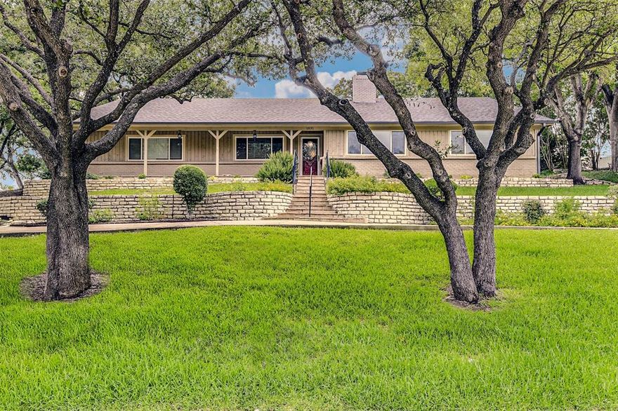 Entertain family and friends in true Texas style in this stunning 4-bedroom 3-bath custom home under the shade of mature oak trees on two hilltop lots in Arlington.  Recently updated, the home is unparallelled in condition with gorgeous hardwood floors adding warmth to the seamless flow throughout.  Dramatic open concept, complete with wet bar, built-in wine fridge and double-sided fireplace to formal dining room, creates an expansive living area for large gatherings.  Expand the entertaining poolside under the large, fan-cooled covered patio overlooking the sparkling saltwater pool.  Totally refreshed gourmet kitchen is a chef’s dream boasting of tons of prep space, delightful island, lighted glass-front cabinets and informal dining area with custom-designed table and banquette with a view of the pool. Large bedroom suites anchor each side of the home with private pool access.  The primary suite offers a private oasis featuring a jetted Roman tub, separate shower and 2 walk-in closets.  Additional living area off entry provides the perfect opportunity for a home office, studio or home school area.  During the hot Texas summer stay cool indoors with the updated HVAC system installed in 2025.  Magical and kept to perfection, all you have to do is move in.
