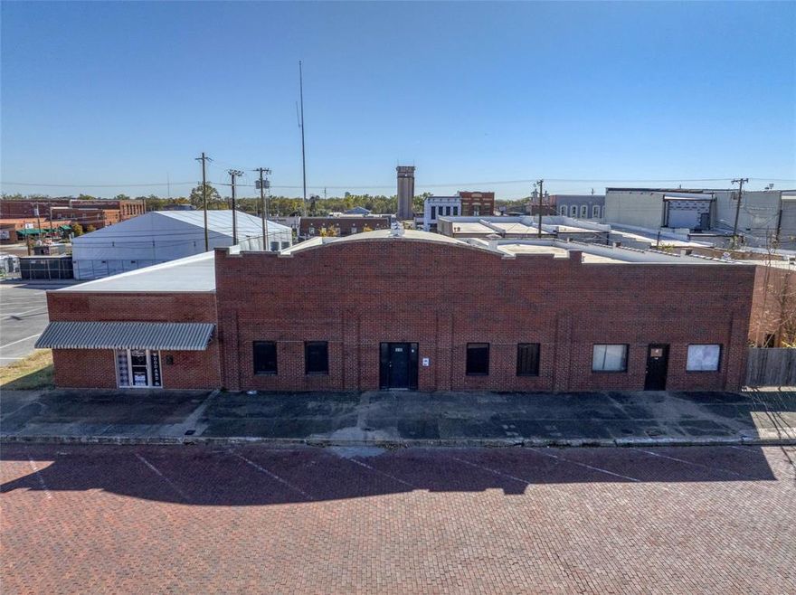 Here is an exceptional opportunity to own a blank canvas in the heart of downtown Denison. This 5,000 square foot shell offers tremendous versatility, supporting a wide range of different uses such as retail, a restaurant, or a modern office concept. The front of the building features several offices, leading into a spacious open area with a uniquely curved roof, high ceilings, and exposed rafters. There is also an overhead door at the back of the building. The building is just one block from Main Street, and there are more than 50 free public parking spaces located just 50 feet to the east (some are temporarily occupied by the seasonal ice-skating rink). Downtown Denison is a recent winner of the 2025 Great American Main Street Award and thrives as a hub for community and commerce. This property presents a rare chance to secure a well-located piece of Denison’s history with unlimited potential.