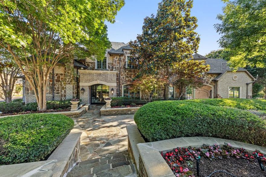 Experience timeless European elegance in this energy-efficient custom manor by Graduate Master Builder Rick McDonald, nestled on over an acre in the prestigious lakefront estate community of Terrabella on Lake Ray Hubbard. Surrounded by majestic oak and pecan trees with serene lake views, this 6,000+ sq ft masterpiece blends old-world charm with modern sophistication. A soaring beamed vaulted ceiling and Juliet balcony crown the grand family room, one of seven fireplaces found throughout the home. The flexible layout includes five spacious bedrooms, five full and two half baths, a private downstairs mother-in-law suite with full bath and its own utility room, a handsome office-library, game room, wet bar, and in-home theatre. The chef’s kitchen is both elegant and functional, featuring dual islands, premium appliances, a pot filler, and a walk-in pantry, seamlessly connected to the formal dining area and butler’s pantry. A custom wine cellar and built-in safe add to the home’s thoughtful amenities. One upstairs bedroom includes a charming loft, perfect as a playroom or study retreat. Outback takes you to a breathtaking covered outdoor living pavilion with fireplace, built-in grill, and dining space, framed by professional landscaping and a dramatic rock waterfall and river feature that creates a peaceful, resort-like setting. Additional highlights include a Porte Cochere, oversized utility room, European chimney pots, abundant storage, prewired sound system, and extensive millwork and custom cabinetry throughout. The primary suite offers a fireplace, spa-inspired bath, and a generous walk-in closet with custom shelving. Multiple zones of HVAC ensure year-round comfort, and energy-efficient construction provides lasting value. This exceptional home offers a rare blend of elegance, comfort, and inspired design just moments from Lake Ray Hubbard.