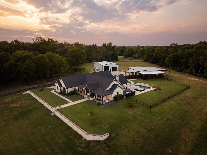 Luxury countryside estate in East Texas! Nestled on 95 acres, this one-of-a-kind luxury farmhouse blends modern smart home technology with timeless country charm, creating the perfect retreat for both everyday living and weekend getaways.Ideally located close to the lakes, this property offers the best of peaceful country living with recreation and modern amenities. The custom-built residence boasts an open floor plan with 3 bedrooms, 2.5 baths, and a dedicated office. Some of the many luxury features throughout include electric blinds and Sonos sound system. Designed for entertaining, the gourmet kitchen features custom cabinetry, quartz countertops, a gas cooktop, double oven, and spacious walk-in pantry with a coffee bar. High-end finishes such as leathered granite, heated flooring, a walk-in shower, bidet, and a custom-built closet system sets the primary ensuite apart. Energy conscious upgrades, including spray foam insulation and a whole-home 24kW generator, provide peace of mind year round. Step outside to enjoy your private resort style amenities: a sparkling in ground pool, hot tub, fire pit, and an outdoor cooking area, all overlooking serene countryside views. A 2.5 acre stocked pond, milesof trails, and the perfect balance of pasture and woods make this property a hunter’s paradise and nature lover’s dream.Additional features include a 3 car garage with epoxy flooring, and two expansive shops: one with a half bath, 2 bay doors, and plenty of storage; the other with spray foam insulation and space for an RV with a pass through door. This exceptional property offers space, privacy, and every modern convenience, all wrapped in the beauty of East Texas. Whether you’re seeking a peaceful escape, a place to work and play, or simply to embrace the quiet country lifestyle, this rare gem delivers it all.