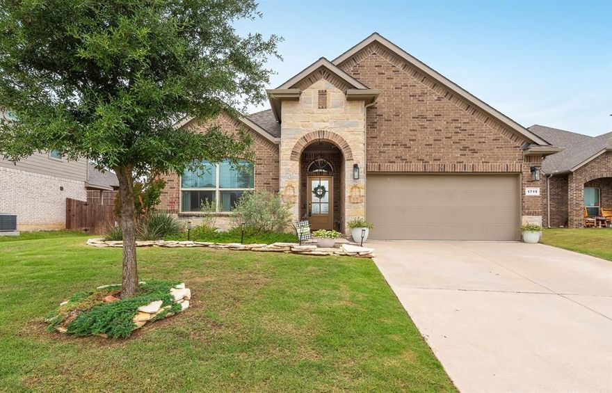 Welcome home to this stunning 4-bedroom, 2-bathroom gem offering 2,064 sq ft of thoughtfully designed living space — move-in ready and loaded with personality from the moment you pull up! Gorgeous brick and stone exterior, mature landscaping, and manicured flowerbeds create undeniable curb appeal that sets the tone for everything inside. The heart of the home is a chef-inspired kitchen featuring an abundance of dark cabinetry, beautiful granite countertops, white subway tile backsplash, stainless steel appliances, and a show-stopping island with geometric tile detail and breakfast bar seating — all illuminated by stylish woven pendant lighting. A walk-in pantry keeps everything organized. The open-concept layout flows seamlessly into the dining area and living room, where decorative wood slats accent the floating TV console, shelves and wood like ceiling fan create a warm, inviting atmosphere. Already wired for your flat screen — just bring it and make it yours! Step through the back door to a covered patio perfect for grilling rain or shine, overlooking a large, fully fenced backyard. A designated office area provides the focus space you need, while three additional bedrooms and a full bath offer flexibility for guests or hobbies. The large laundry room offers additional storage, keeping life running smoothly. Retreat to the spacious primary suite, where a striking teal board-and-batten accent wall sets a serene, designer tone. The ensuite bath impresses with new dual sinks, a soaking tub, walk-in shower, and an impressive walk-in closet. Located in a sidewalk-lined community with scenic ponds and walking paths, with quick access to Hwy 377 — a seamless commute whether you're heading downtown or to the Metroplex. New Roof in 2025, added gutters, exterior light fixtures & more. Everything has already been done for you — just unpack and enjoy!