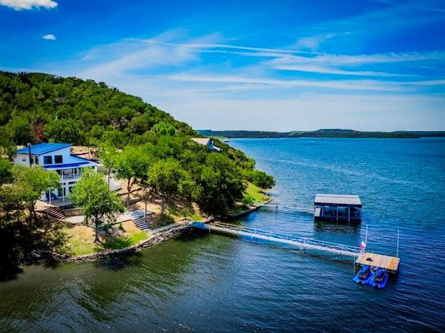 BREATHTAKING 'BURMA BLUE', CONTEMPORARY, FURNISHED, WATERFRONT 5BD, 3.5BA, 3420SqFt LAKEHOUSE on the Peninsula at PK, with Sparkling Blue Waters on the Broadway of Possum Kingdom Lake. Nestled in the N.Tx Hill Country, this Prime Peninsula Location is close to both the West and East sides of PK as well as to the Amenities & Dining nearby by Car or Boat, and accesses the miles of Hiking and Biking Trails off Burma Rd. This Custom Modern, Light & Bright Home has a great Open Concept Design Floor Plan, Perfect for all your Lake Entertaining and Fun, and has been an Excellent VRBO Rental as well. The House also Features 2 Living Areas for multiple families and has a Wonderful Game Room and Bunk Room on the Lower Level, all with Beautiful Lake Views from Walls of Windows throughout the house and off the Covered Porches. The Views from the Main Level Living Room and the Primary Bedroom are absolutely Stunning, and the Spectacular Sunsets and Tx Starry Nights, are Unparalled. Outside there is a Covered Outdoor Seating Porch with Panoramic Lake Views, & a Patio with Outdoor Kitchen, Dining, & Seating with TV area & Fireplace, and then just an easy walk down to the Lake, is a Wonderful Area for Relaxing & Recharging on the Waterfront with room for Yard Games, Fantastic Fishing, and Roasting S'mores on the Fire Pit, and then its just a short distance to get the Walkway to the DEEP Water Platform with Boat Whips and 2 Jet Ski Ports. This Amazing Oasis Lake Retreat, known as 'Burma Blue', is waiting for you.....