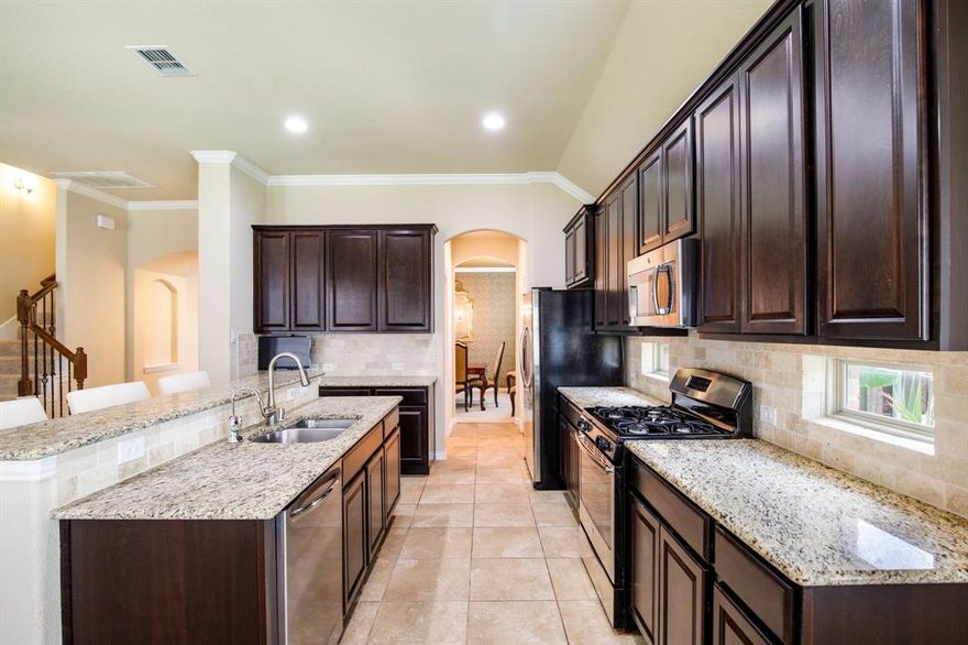 This beautiful corner-lot home is tucked away on a quiet cul-de-sac in McKinney’s sought-after Inwood Hills neighborhood. From the moment you step inside, you’ll notice the natural light, open spaces, and thoughtful design that make this home so comfortable and welcoming.
A two-story foyer opens to a stylish dining room featuring designer wallpaper, statement lighting, and an accent ceiling that adds character and charm. The kitchen is the heart of the home, complete with granite countertops, stainless steel appliances, a gas range, and a large island with breakfast bar seating. It flows easily into the spacious living area, where large windows and a cozy fireplace create an inviting place to gather.  The breakfast nook just off the kitchen leads to a covered patio-perfect for coffee in the mornings or casual dinners outdoors.
The primary suite is located on the main floor and serves as a peaceful retreat, offering dual sinks, a soaking tub, a separate shower, and a walk-in closet. Also downstairs, you’ll find a guest bedroom with a full bath that’s ideal for visitors or a dedicated home office. Upstairs, there’s room for everyone to relax or play, with a large game room featuring window seating, a media room for movie nights, and two additional bedrooms that share a full bath.
Step outside to a backyard built for both relaxation and fun. The covered patio is perfect for entertaining, while the stone firepit area offers a cozy spot to unwind under the Texas stars.
The location is another highlight- just minutes from El Dorado Country Club with golf, dining, and social activities, and close to Bonnie Wenk Park with walking trails, a dog park, and community events. This home is also zoned to top-rated McKinney ISD schools and part of the Inwood Hills community, which features a pool, playground, and tree-lined walking paths.