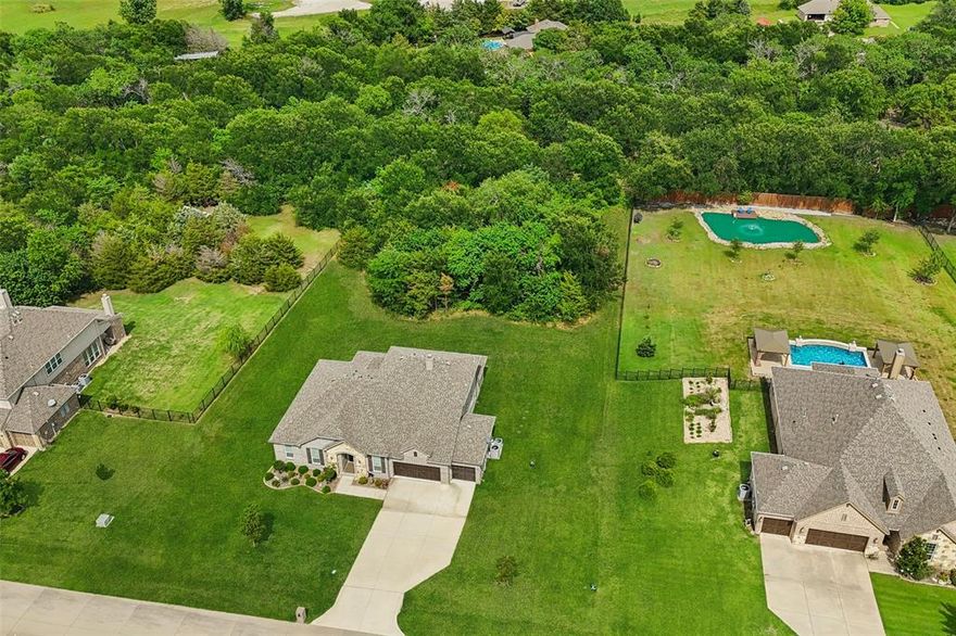 Nestled on over 1 acre of serene, wooded land in a private gated community, this beautifully designed modern ranch home blends luxury and functionality in a peaceful natural setting. From the moment you enter through the stunning wood and iron front door, you’ll be welcomed by soaring ceilings, an abundance of natural light, and elegant wood flooring throughout. The open-concept kitchen is a chef’s dream, featuring a large center island with bar seating, granite countertops, crisp white cabinetry, stainless steel appliances, a 5-burner gas range with a custom wood vent cover, and recessed lighting. The spacious living area centers around a striking stone-surround fireplace with a cedar mantel—perfect for cozy evenings or entertaining guests. The thoughtful floorplan includes a private home office with French doors, an inviting game room, and a guest suite with a bedroom and full bath upstairs. The primary suite offers a spa-like retreat with an oversized walk-in shower with a built-in seat, a luxurious soaking tub, a double quartz vanity, and a large walk-in closet. Additional highlights include an iron spindle staircase, tankless water heater, and a fully equipped laundry room with quartz countertops, a sink, and built-in cabinets. Spacious covered back patio, ideal for relaxing or hosting gatherings. This easy-to-maintain home is perfect for both family living and entertaining. Refrigerator, washer, and dryer will stay with home. Large TV is negotiable. Enjoy the comfort, privacy, and beauty of nature—all within a welcoming, well-maintained community. 3D Tour available online.