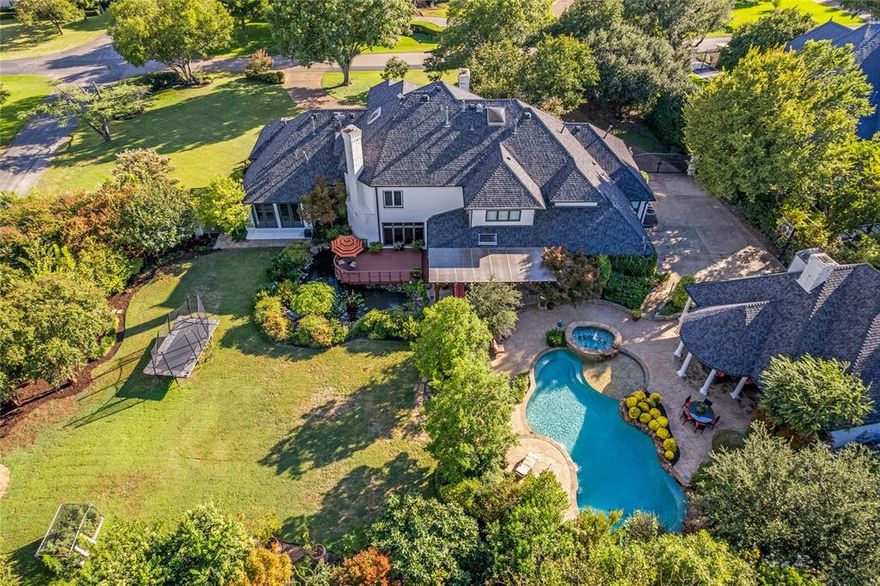 This extraordinary private estate spans 1.08 acres in one of Dallas’ most prestigious neighborhoods & is designed for outdoor living & entertaining. The grounds showcase a park-like setting with a 4000-gallon koi pond with more than 50 fish, 2 waterfalls, & an observation deck. With no neighbors on one side, the beautifully landscaped ppty ensures exceptional privacy. Multiple outdoor living areas invite year-round entertaining. The resort-style backyard features a pool & spa with pool bath, 2 pergolas, fireplace, kitchen-54” Wolf grill, sink, & fridge. Separate gated multi-purpose space offers endless possibilities. Professional landscape lighting, mature trees, & expansive lawns complete the setting. Inside, the transitional-style home blends timeless elegance with modern luxury. It offers 5 bedrooms, 6 baths, plus 400sf detached qtrs with bedroom, ensuite, and kitchenette. The chef’s kitchen is anchored by a spacious island, Sub-Zero refrigerator, Wolf 6-burner cooktop, Miele double ovens, steam oven, warming drawer, microwave-third oven, 48-bottle wine fridge, dual sinks, dual dishwashers, & custom cabinetry. A main wet bar with copper sink, ice maker, and decorative cabinetry complements the space, while a 200-bottle temp-controlled wine closet & dining room with courtyard fountain views elevate entertaining. The downstairs primary suite overlooks the backyard with a wall of windows & french doors. Addtl spaces include a private office with a view of the koi pond, oversized den with wet bar & ensuite, hidden craft room, & media room with theater seating, wet bar, and half bath. Recent updates include spa-like primary bath and a secondary bedroom featuring dual closets. Luxury finishes include 3 fireplaces, surround sound indoors & out, 4-car garage (2 & 2), motorized gated courtyard, security cameras & 30-day DVR system, & optional Royalwood Armored Patrol services available. House has the advantage of the latest technology.