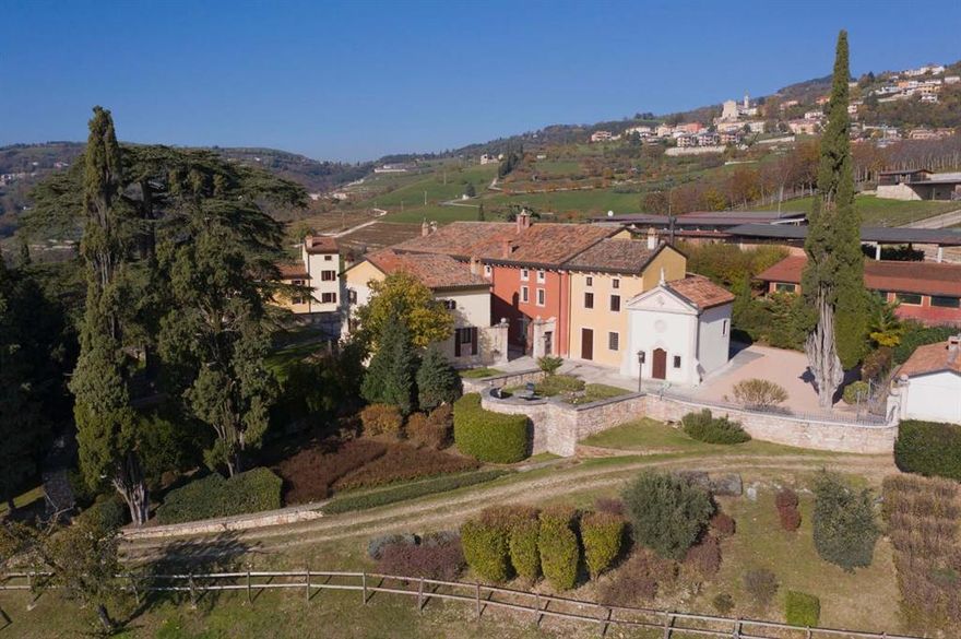 Set in the gentle rise of the Veneto hills, where vineyards meet the foothills of the Alps, this 15th-century estate once belonged to a noble Veronese family. Its past lives in fresco traces, arched loggias, and sunlit courtyards, restored with care to blend heritage with modern comfort. Morning light warms the terracotta rooftops and manicured gardens, while evenings carry the scent of cypress, reminding you that beauty here is felt as much as seen.
   Passing through the gates, time seems to slow. Hand-hewn stone, classical proportions, and tall windows create a calm, inviting atmosphere. Vaulted ceilings, old beams, and soft natural light give every room a sense of quiet nobility. From the grand salon to the shaded loggias, each space feels designed for gathering, lingering, and living well.
   Beyond the villa, the land opens into vineyards, orchards, and silvered olive groves that have shaped local life for centuries. Just outside Verona, the estate enjoys rare privacy while remaining close to the region’s cultural heart. Days begin with church bells carried on mountain air and end with wine from the vineyards as the hills shift to evening gold. Lake Garda, the Dolomites, and Verona’s art and architecture are all within easy reach.
There are places that spark the imagination, and others that settle into the heart. La Pavarana does both. It carries its history lightly, offering a life measured not in hurry, but in moments — footsteps on cool stone, afternoon light across a wall, laughter under a canopy of stars. For those seeking more than a residence, La Pavarana is a rare inheritance: a home, a landscape, and a way of life.