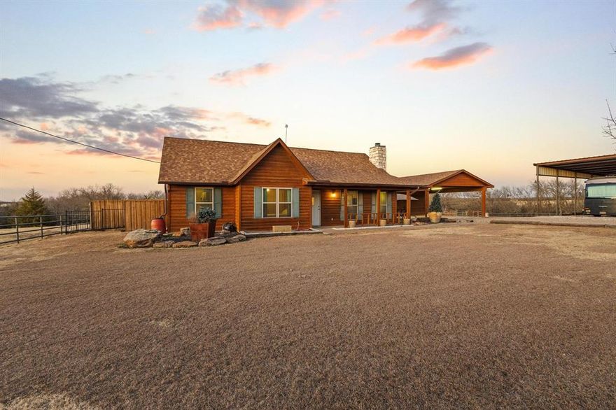 Experience the ultimate Texas sunset from this private 18+ acre oasis. Whether you’re soaking in the hilltop pool, unwinding on the expansive patio, gathered around the firepit, or relaxing in the hot tub, you’ll enjoy evening panoramic vistas that put you front-row to the best show in North Texas.
Bathed in natural light & curated with impeccable style, this breathtaking home offers sweeping views that create the perfect backdrop for everyday living. Designed for seamless indoor-outdoor flow, the open-concept layout centers around a striking stone fireplace, creating a warm, inviting atmosphere that opens effortlessly to multiple outdoor entertainment spaces. The kitchen offers endless counter space & large island with seating making hosting a breeze, flowing into a dramatic dining area with soaring ceilings & a picture window frames stunning pool & ranch views. The home was originally designed as a three-bedroom & has been thoughtfully converted to a spacious two-bedroom layout, enhancing the living areas while maintaining comfort & functionality. Two generously sized bedrooms & two full baths provide quiet retreats to end the day. Detached flex space offers excellent versatility & would make an ideal home office, gym, studio, or creative workspace. The courtyard extends across the back of the home, leading to a hot tub, sauna, & fenced pool area—perfect for relaxation & entertaining. Outdoor amenities include a covered RV area with water and a 50-amp hookup & designed to be easily converted into a full-size pickleball court, an impressive six-stall metal barn with wash rack, tack room, electricity, & water, plus a nearby corral with water access. Pastures are fenced & cross-fenced, complemented by a stock tank & mature trees. Currently ag-exempt, this ranch is comfortable, functional & ready for your livestock. This isn’t just a ranch—it’s a lifestyle.