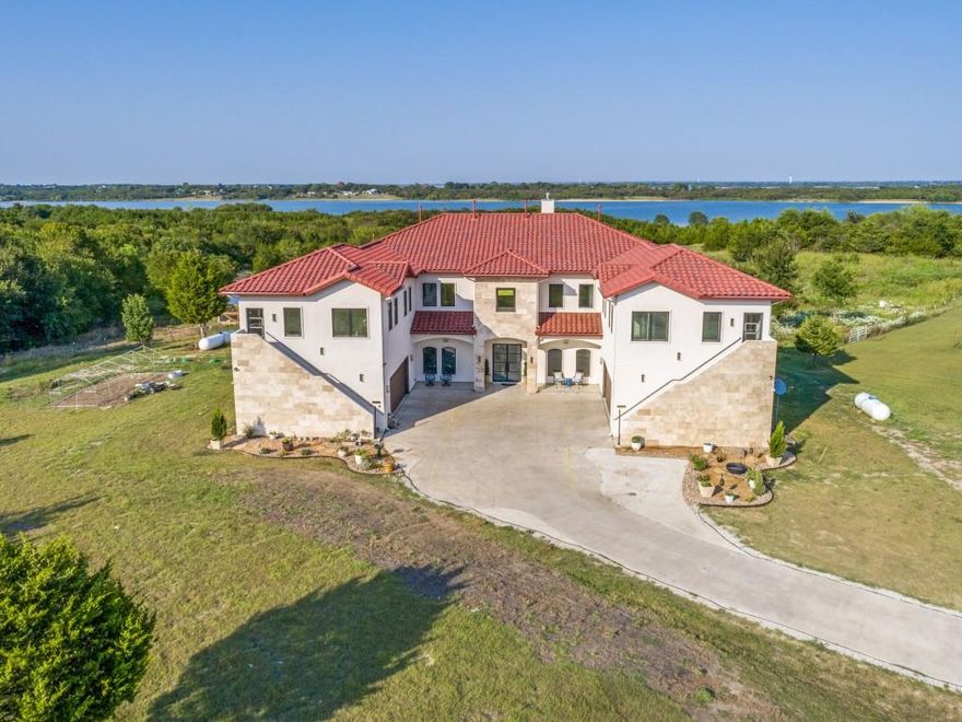 Custom multi-generational estate situated on over 4 acres of beautiful unincorporated property adjoining Corps of Engineers land on Lake Lavon! This Mediterranean-inspired home comprises 6 bedrooms, 7 bathrooms, 5 kitchens, 4 living rooms, 4 dining areas, 2 offices, media room, & game room - a unique layout offering functionality, privacy, & accessibility without compromising a sense of community & inclusion. Both upstairs wings of the home feature their own private exterior entries that lead into living rooms with kitchenettes for independent living. The front entry features double glass doors that welcome you into the foyer flanked by the light-filled dining room & the curved staircase with wrought iron balusters. The living room enjoys a focal gas fireplace & picture windows for scenic views. Right off of this gathering space is a guest bathroom & game room which could also be used as a hobby room or exercise room. A media room with stadium-style seating provides an additional entertaining space. A dedicated home office with built-in cabinetry offers a tranquil environment for remote work. The main kitchen features a built-in refrigerator & freezer, commercial gas range, vented hood, quartz waterfall island with storage, an abundance of cabinets, glass mosaic tile backsplash, & pot filler. A true chef’s kitchen with a huge walk-in pantry is just around the corner creating the perfect place for no-fuss meal prep. Guests staying overnight will appreciate the private downstairs guest suite. Upstairs you’ll find an incredible living room with a kitchenette that anchors the primary suite & four additional bedrooms with gorgeous en suite bathrooms. LVP flooring throughout the main living areas & bedrooms! Both garages are plumbed for an additional washer & dryer & include 2 universal EV charging stations. Exquisite lakeside living surrounded by the sounds of nature, views of the water, & acreage for cows, horses, goats, & chickens!