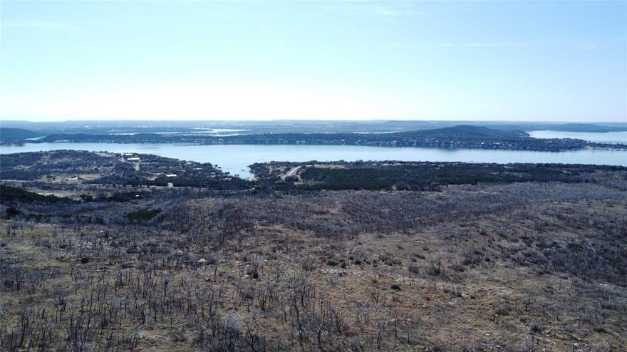 An exceptional opportunity to acquire 320± acres overlooking Possum Kingdom Lake in the heart of Palo Pinto County, featuring Caudill Mountain, a named county summit rising to approximately 1,360+ feet in elevation. This unique high point offers commanding views of Possum Kingdom Lake on one side and a sweeping valley panorama on the other, creating a rare dual-aspect vantage seldom found on privately held ranch land.
The property showcases dramatic topography with rolling hills, rugged slopes, elevated ridgelines, and scenic high points that provide expansive views from multiple locations. Native oak, mesquite, and cedar blend with open pasture and grassed areas, delivering both visual appeal and functional grazing capacity. Two established stock tanks and a water tap enhance the ranch’s recreational and agricultural utility, supporting wildlife and livestock operations. The property benefits from an existing agricultural exemption and is well-suited for cattle operations, hunting, recreational use, and future residential development. The ranch also includes a cellular communications tower generating approximately $500 per month in rental income, with all electrical service and related utility costs paid by the tower operator, providing supplemental passive revenue. With approximately 2,000 feet of FM road frontage, access is provided via an all-weather road and available co-op electric service. The ranch is unzoned and unrestricted, allowing flexibility for a private estate, legacy ranch, recreational retreat, or long-term investment holding. Wildlife is abundant, including whitetail deer, hogs, dove, ducks, and native game species. The varied terrain and vegetation create diverse habitat and natural cover throughout the property. This is a rare opportunity to own a landmark-quality ranch centered around one of Palo Pinto County’s signature high points—offering elevation, views, privacy, income potential, and versatility in a premier Possum Kingdom Lake setting.