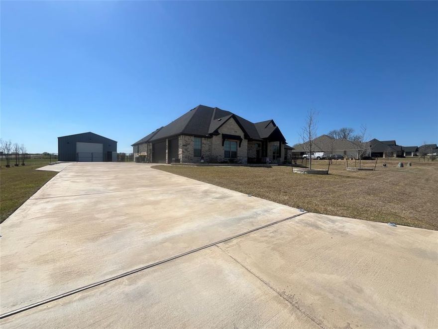 If you are looking to live OUTSIDE THE CITY LIMITS in a spacious, almost new, 1-owner country home offering WONDERFUL curb appeal along with a 1,200sf insulated workshop boasting 14ft walls and 12ft powered Overhead doors on a 1-acre fenced and cross-fenced lot, you have come to the right place! Approaching the home, notice the beautiful brick and rock work as well as the fantastic wood accents. Observe the meticulous design and care that has been given to the gardening beds bordering the home's facade complete with a relaxing covered porch. Enter to find the office conveniently located to your left through the French Doors. The entry hall opens to an expansive open floorplan connecting the living room, dining room, and kitchen all with lofty ten foot ceilings. A charming WBFP is located opposite the entry hall and overlooks the living area. The kitchen exhibits class with walls of floor to ceiling solid wood custom cabinetry accompanied by undermount lighting and hidden built-in spice racks, granite countertops, ss appliances, walk-in pantry, and 9ft island. The master bedroom offers a great view of the backyard and space for a sitting area. The ensuite bath is massive with a large garden tub and separate shower, dual vanities with a make up prep area and more than 15 feet of counter space.  The home can be set up as a 4 bedroom with an office or a 3 bedroom with a 2nd family room and an office as it is currently. The 4th bedroom is 16 x 15 and has ensuite half bath that has private entrance to the backyard and its covered patio making it perfect if you would like to add a pool! The oversized attached garage is approximately 720sf with a depth of 24ft and raised 8ft garage doors to accommodate large vehicles.  New 30-year roof installed in 2025; high-speed fiber optic cable service; security cameras and security system stay with the home; 2in faux wood blinds throughout; decorative lighting; mudroom just off garage; desirable Maypearl ISD…well worth visiting!