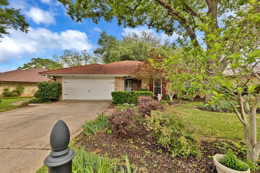 Located in a highly desirable, established neighborhood, this charming brick home is surrounded by mature trees and timeless character. Inside, you’ll find real hardwood flooring, tile, and carpet throughout, along with a beautifully updated kitchen featuring granite countertops, abundant cabinetry, bright lighting, stainless steel refrigerator, built-in microwave, and stylish tile flooring. The main living area is filled with natural light thanks to skylights and accented with warm wood beams. A cozy wood-burning fireplace also adaptable for propane adds comfort on winter days. The home has been exceptionally well maintained, reflecting the pride of ownership. The spacious primary bedroom includes a large walk-in closet and a full ensuite bath with an updated separate shower. Additional bedrooms offer generous closet space and ceiling fans. Major upgrades include a durable metal terracotta-style roof with a 50-year warranty and newer windows. A standout feature is the gorgeous covered patio, complete with large windows and lovely tile flooring perfect for relaxing or hosting gatherings year round. The property also includes a two-car garage and a seperate utility room with a washer and dryer. Situated close to schools, restaurants, shopping, DFW Airport, museums, and countless activities, this home offers both convenience and charm in an unbeatable location.