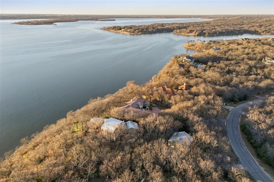 Architecturally distinctive Lake Lewisville waterfront residence situated on a 1.44-acre elevated peninsula in the Emerald Sound community, offering exceptional privacy, panoramic lake views, and direct access to the water. Designed by GGOArchitect Gary Olp, the home reflects a thoughtful integration of passive solar design, sustainable materials, and site-responsive architecture that preserves mature Texas native trees.

Expansive south- and east-facing windows with architectural overhangs provide abundant natural light while supporting year-round energy efficiency. Strategically placed north and west openings contribute to balanced interior climate control. Five Andersen double-pane glass door systems connect interior living spaces to gardens, patios, and lake views.

The cantilevered primary suite extends toward the shoreline, creating a private retreat with sunset views over the lake. Outdoor living areas include a Rumford fireplace, a sunken stone patio kitchen, and a landscaped spa setting surrounded by drought-tolerant plantings and herb gardens. A constructed pathway leads to the water’s edge with kayak storage and convenient lake access.

The exterior features cementitious stucco, ICF construction, and a standing-seam metal roof, offering durability, sound insulation, and thermal performance. The lower level provides additional storage and a temperature-controlled wine cellar. All bathrooms throughout the home have been updated, and the kitchen is enhanced by brand-new appliances, including dual ovens. A second-floor Eagle’s Nest loft features a widow’s watch window.

The property includes a four-car garage with a private guest suite offering an ensuite bath, walk-in closet, and light kitchenette designed for beverage and snack preparation. A rare opportunity to own a design-driven, energy-efficient waterfront home in one of Lake Lewisville’s most private and elevated settings.