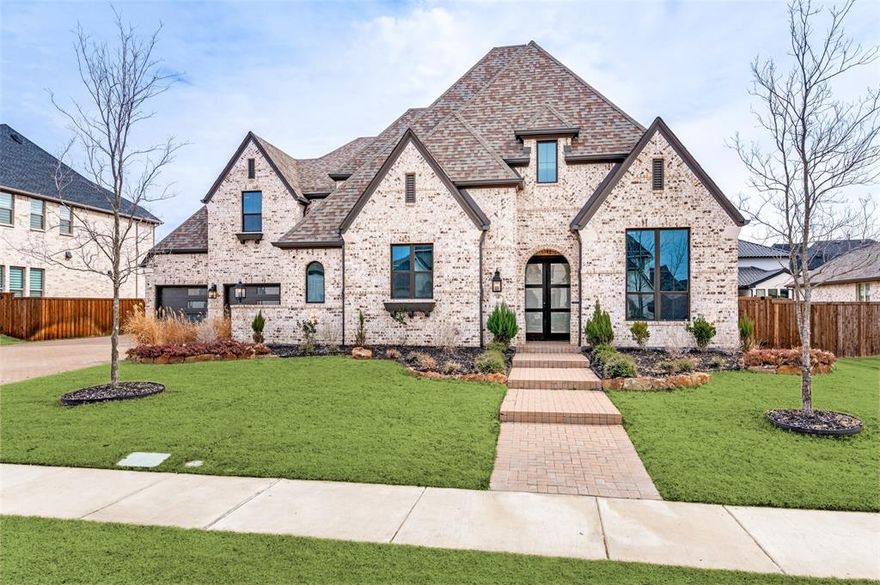 Highland Home located in Prosper’s highly acclaimed school district, this exceptional residence offers refined design, resort-style amenities, and peace of mind with a 10-year builder and structural warranty in place. A rare 4-car oversized garage is a true showpiece, featuring modern metal and glass garage doors and motion-sensor hexagon lighting for striking architectural appeal and superior functionality. The private backyard showcases a resort-style pool installed in 2024, currently under warranty, with a gradual 3.5–6 ft depth, an 8-person spa, and a sauna that conveys, complemented by a covered patio with fireplace for year-round enjoyment. Inside, Level 6 Costa Brava Andora flooring flows throughout, highlighted by a dramatic herringbone entry. The statement staircase features solid wood steps and landing, stained true black, complemented by an Iron Ore  railing and a custom baluster wall design. The family room is anchored by a floor-to-ceiling polished quartz slab fireplace surround, creating a stunning focal point.
The chef’s kitchen impresses with double ovens, a professional-style cooktop, oversized island with 4-inch quartz waterfall edge, full-height quartz slab backsplash, and a quartz slab vent hood, with custom tile details continuing throughout. Designer lighting, upscale hardware, and statement faucets elevate every space, while electric custom shades enhance both the family room and primary suite. The primary retreat offers a sitting area, split vanities with 3-inch quartz countertops, a spa-inspired soaking tub and separate shower, and a thoughtfully designed walk-in closet with generous hanging space and custom features for two.
Additional highlights include an oversized laundry room with sink, folding space, and abundant cabinetry, a downstairs media room and private office with French doors, plus an upstairs game room and three secondary bedrooms—each with its own private bath—along with exceptional storage throughout.