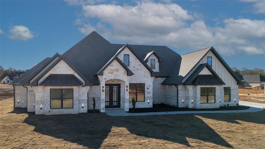 12325 Madison Crossing Bullard, TX !  Stunning and breathtaking, this custom new construction is sure to impress. Located in one of Bullard’s newest subdivisions, this exceptional home blends timeless charm with modern design from the moment you arrive. Eye-catching curb appeal features a striking combination of stone, brick, and siding, complemented by high-pitched roofs and dramatic gables. Step through the 8-foot double iron front doors into a unique foyer with bold, elegant color selections that set the tone for what’s to come. The expansive living area showcases a cathedral-style ceiling, rich maple cabinetry, and custom built-ins flanking a stunning floor-to-ceiling stone fireplace, creating a warm yet luxurious focal point. The chef’s kitchen is equally impressive, offering floor-to-ceiling cabinetry, a spacious hidden pantry, and stainless steel appliances including a gas cooktop, built-in oven, microwave, dishwasher, and a tankless water heater for efficiency and comfort.
The primary suite is a true retreat, featuring a beautifully designed box-top ceiling with beams and a spa-inspired bathroom complete with double vanities, a soaking tub, a walk-in shower with multiple shower heads, and a generous walk-in closet. This home offers 4 bedrooms, including one that functions perfectly as a mother-in-law suite with its own full bath. An additional dedicated office or study with custom built-ins adds versatility and convenience.
Step outside to the oversized covered patio and outdoor kitchen—perfect for entertaining or relaxing. The space includes granite countertops, a sink, built-in grill, and wine cooler, making outdoor living effortless and enjoyable. All of this sits on a level half-acre lot, offering both space and privacy.
This impeccable new build delivers modern design, thoughtful details, and luxury throughout. Schedule your private tour today and call your favorite REALTOR to experience this stunning home in person.