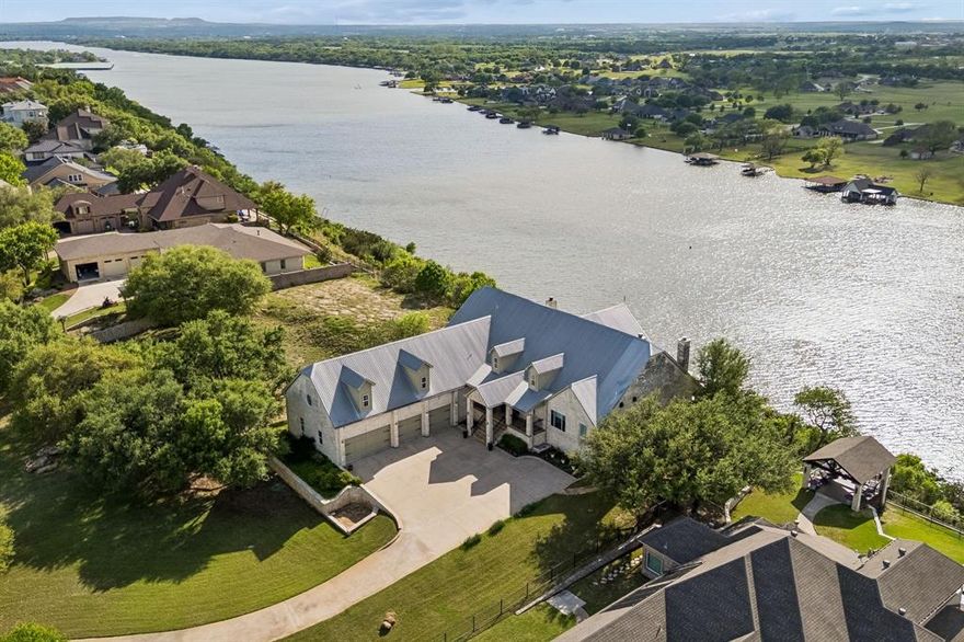 Perched atop one of the highest elevations on any North Texas lake,this exceptional property showcases sweeping 180° dramatic views of the Brazos River Bend & Lake Granbury! The elevated setting offers rare privacy, presence, and panoramic western sunset views, an uncommon vantage point in Granbury plus a private tram leading directly to your multi-slip exclusive dock below. The open-concept living spaces capture expansive views, & the home features 5 ensuite bedrooms & 2 powder baths (one conveniently located off the pool terrace). The recently updated chef’s kitchen is designed for both everyday living & entertaining. Kitchen has a large Sub-Zero refrigerator & Thermador 6-burner range with grill & double oven, Sub-Zero beverage fridge & U-line ice maker. The kitchen flows into the dining & living areas, boasting a wall of Anderson windows & French doors. Outdoor living ia resort-style experience with a central primary deck leading to tiered spaces that include a built-in pool with swim-up bar seating, a separate 4-seat hot tub lounge and patio, & multiple areas for grilling, dining, & relaxing with maximum views. Dual staircases provide access from the oversized 4-car garage & between levels, including a private upper retreat ideal for guests or multi-generations. The primary suite is approximately 600 sq. ft., with a fireplace and a remodeled bath featuring an oversized shower, heated floor & towel rack, and an enormous custom closet with a full mirrored wall. This primary suite has its own fireplace in the room & also opens to an outdoor terrace with a fireplace and an outdoor TV! Another large bedroom also opens to the upper terrace, with easy access to the hot tub sundeck patio below. The epoxied oversized 4-car garage  & extended driveway provide ample parking. A unique blend of elevation, privacy, panoramic views, and thoughtfully designed indoor-outdoor living makes this property truly one of a kind.  See more information in the MLS document section