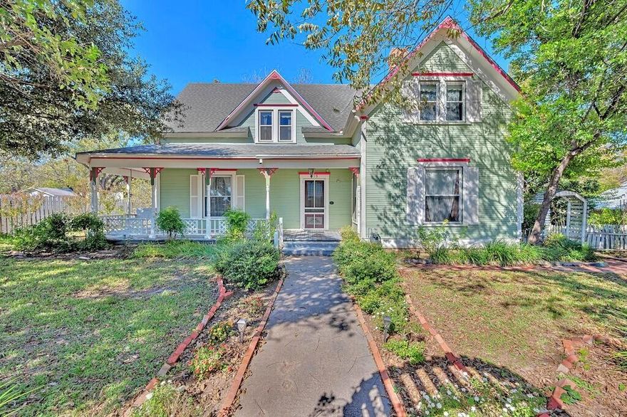 On a wide corner of Clifton, a Victorian with pink trim and a wraparound porch has been quietly gathering stories for more than a century. Morning light filters through lace curtains, the porch swing creaks, and the path leads you to tall doors that open into rooms meant for company, holidays, and slow afternoons. Downstairs moves the way an old soul should: a front parlor for piano and conversation, a formal dining room that begs for china and candlelight, a cozy living room anchored by a gas fireplace, and a generous kitchen with painted cabinets, bead board, and room to spread out. There’s a true pantry, a separate laundry-mudroom, and even a small hideaway under the stairs that makes the perfect storage nook or child’s secret fort.

Up the staircase, sloped ceilings and dormers shape intimate spaces. Three bedrooms sit alongside a charming “getting-ready” room with its own ensuite. It’s easy to picture quilt stacks, hat pegs, and the sort of mornings where everyone moves at their own pace.

The practical pieces are handled. New windows were added in 2006. The home was leveled in 2008. Blown insulation upstairs and spray foam beneath the floors temper Texas seasons. 

Outside, the property stretches across two city lots with room for gardens, swings, and the Saturday project list.  Two outbuildings stay useful—a garden shed (8×10) and a larger storage building (12×20) with a half loft and a 220 plug for tools. There is a detached two-car garage with an  carport for extra cover.

It’s the rare blend here—history you can feel, space that works for real life, and thoughtful updates where they matter. If you’ve been waiting for a Clifton Victorian with good bones and a big heart, this is the one that lets you slow down, spread out, and start your next chapter on Hackberry.