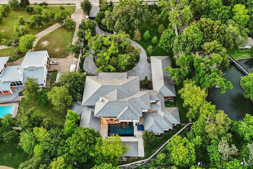 Modern Italian design meets Texas swagger on nearly 1.8 gated acres in the heart of Preston Hollow. Built in 2017 by Sharif and Munir Custom Homes and designed by L. Lumpkins Architects, this breathtaking estate offers 9,406 square feet in the main house plus two completely private guest quarters, each with a bedroom, bath, living area, and kitchen. The grand 25-foot front loggia with coffered ceiling and three iconic Italian arches sets the tone before you ever step inside. Once you do, soaring ceilings, floor-to-ceiling windows, and interiors by RN Interior Design create a home that is simultaneously sleek, warm, and completely unforgettable. The entertainer's floor plan is unmatched at every level. Dual Italian marble islands, Wolf and Subzero appliances, and a thoughtfully designed back area with prep kitchen, storage, and laundry create seamless entertaining flow. Two bars, a game room upstairs, and multiple flex spaces mean there is always a perfect setting for any gathering, any mood, any occasion. The great room opens through 14-foot sliding glass walls directly to an infinity-edge pool, and the indoor-outdoor flow continues seamlessly to resort-style living with a full cabana, gas fireplace, and grilling station. The entire property was designed so entertaining never stops at a door. The primary suite features a spa bath with heated marble floors, dual shower, freestanding soaking tub, and a private gym. Custom ceiling details with ambient lighting glow throughout the home, creating warmth and sophistication in every room. Geothermal systems, Control4 automation, and a whole-home Generac generator round out the infrastructure. A property designed for how people actually live. Hidden from the street by a full acre of mature trees, this is complete privacy within the city. Unmatched entertaining infrastructure, sleek design, and rare Preston Hollow acreage combine in one of Dallas' most distinctive estates.