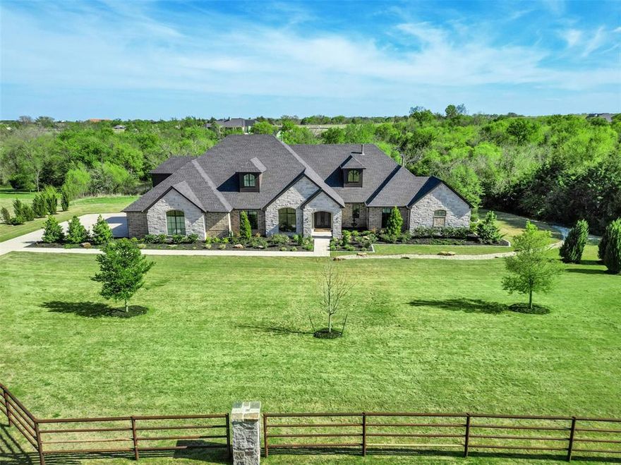 In The Prestigious Hills of Lone Star – where country is the theme for easy living. Set against a beautiful tree-lined backdrop, this property offers privacy and generous elbow room. Thoughtfully designed with over 7,300 sq. ft., including more than 5,000 sq. ft. on the first level, this home was made for entertaining. The expansive kitchen is the heart of the home and is complete with every convenience for the cook, including a large entertaining island, gas cooktop, private dining area, scullery kitchen, and generous walk-in pantry. Open to the great room is a beautifully appointed wet bar room, creating a natural gathering space with lovely backyard views—perfect for making memories with friends and family. The private owner’s suite features a separate sitting area, peaceful views, a Texas-sized bath, and separate closets. Three additional guest suites with private baths are located on the main level, including a mother-in-law suite with its own sitting room. Greet the morning with coffee or spend a quiet afternoon in the nature-filled sunroom located off the secondary living-flex space with fireplace. Completing the first level are a private study and a spacious utility room with space for multiple washer and dryer sets. Step outside under the Texas sky and enjoy year-round living with a covered patio, built-in outdoor kitchen with smoker, and an enormous pool-ready backyard. The second level becomes a destination for relaxation and fun, featuring a spacious game and living area, flex room, oversized wet bar for entertaining, and a large balcony perfect for watching both sunrise and sunset. A second flex area is ready for a private gym, additional storage, or play space. This is a smart home that also includes a four-car garage and abundant storage throughout. When you are ready for a night out, take a short country drive to Celina or downtown McKinney, where the food is fabulous, and the shopping is fun.