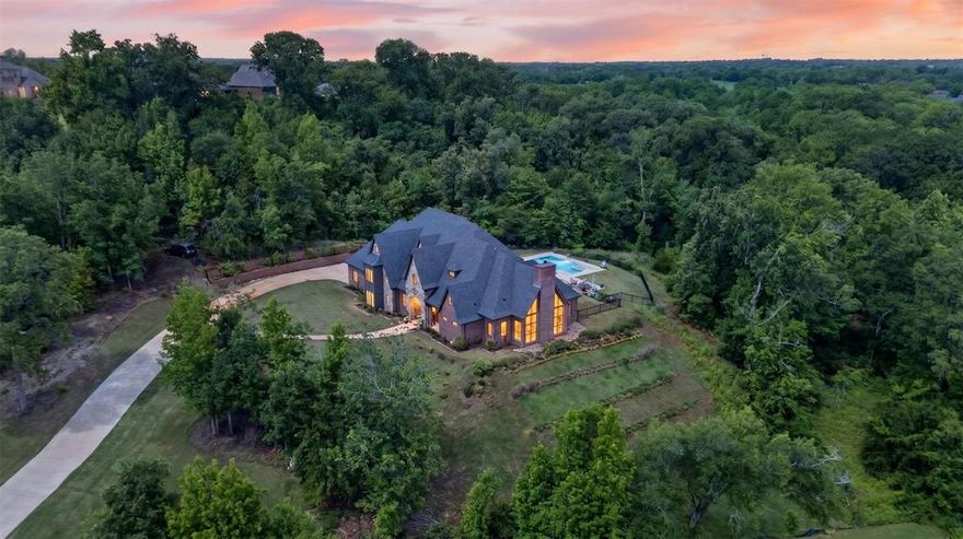 Ever dreamed of living in a castle on a hill overlooking a private lake? Welcome to this breathtaking 5-bedroom, 4-bath luxury estate tucked inside the gated community of Pecan Valley Ranch. Perched above the rolling landscape and surrounded by mature trees on 3.99 private acres, this extraordinary home offers the perfect blend of elegance, privacy, and peaceful East Texas beauty. From the moment you arrive, the stunning architecture captures your attention with soaring rooflines, rich stone and brick accents, dramatic windows, and timeless character straight from a storybook. Inside, natural light pours throughout the home, highlighting the spacious open-concept design and creating warm, inviting spaces at every turn. The gourmet chef’s kitchen was designed to impress, featuring premium gas appliances, custom cabinetry, expansive countertops, abundant storage, and a reverse osmosis water system. Whether entertaining guests or enjoying a quiet evening at home, this space is both functional and luxurious. The spacious primary suite offers a peaceful retreat, while the additional bedrooms provide flexibility for family, guests, office space, or hobbies. Every detail throughout the home reflects thoughtful craftsmanship and upscale finishes. Step outside into your own private resort-style oasis. The stunning pool and hot tub are surrounded by peaceful wooded views, offering incredible privacy and the perfect setting for relaxing evenings, entertaining, or simply soaking in nature. Expansive outdoor living spaces create an atmosphere that feels secluded, serene, and unforgettable. Situated on a beautifully elevated lot with a 3-car garage and surrounded by nature, this property offers the rare opportunity to enjoy refined living while feeling worlds away from the everyday. With breathtaking views, incredible natural lighting, luxurious amenities, and one of the most picturesque settings in Bullard, this home is truly one-of-a-kind.