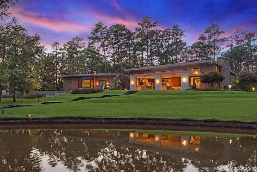 A rare offering—this extraordinary contemporary estate sits on 12 breathtaking acres just beyond the city limits, delivering unmatched privacy, architectural distinction and refined modern living. Surrounded by sweeping natural beauty and tranquil water views, the property offers a remarkable retreat while remaining conveniently close to town. A dramatic cypress and steel entry canopy frames the custom mahogany front door, setting the tone for the home’s striking architectural design. Inside, expansive living spaces are defined by soaring ceilings clad in rift-cut white oak and anchored by a site-built linear fireplace with a Basaltina hearth, creating a warm yet sophisticated atmosphere in the Living Room. The Chef’s Kitchen is both beautiful and functional, thoughtfully appointed with double islands, prep sink, two Bosch dishwashers, a Miele built-in coffee system, a double Wolf range and additional oven. Seamless indoor-outdoor living unfolds as the main living areas open to a stunning Outdoor Living Area complete with a fully equipped outdoor kitchen, ceiling heaters and electric screens, allowing the space to be enjoyed year-round. The private Master Suite is a true sanctuary, offering a dedicated Office, Fitness Room and a spa-inspired Bath overlooking the peaceful pond and pool. The stocked pond provides exceptional fishing and recreation just steps from the home. Designed for both luxury and practicality, the property features private well water, septic system, a whole-house generator and the added benefit of no city taxes. Smart home features include an ELAN sound system, Storm Room and extensive system upgrades completed in 2020. Outdoor amenities further elevate the property with a heated pool and cover, irrigation system and fencing for privacy. The land attracts abundant wildlife, with deer and even bald eagles known to visit. A truly exceptional estate offering privacy, modern innovation and connection to nature—an unparalleled lifestyle opportunity.