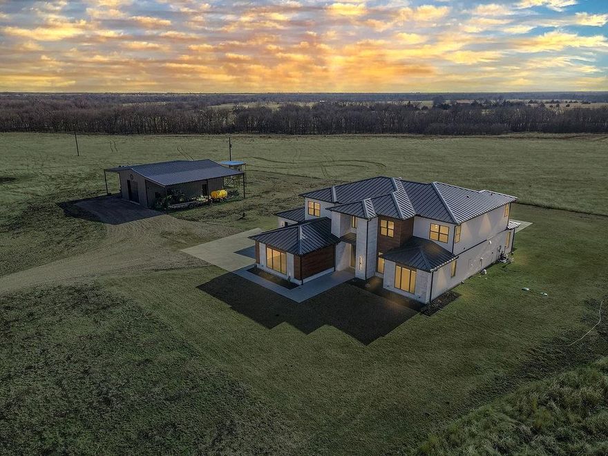 Set across 163 breathtaking acres of rolling East Texas countryside, this exceptional transitional-style custom home blends refined architecture with the freedom and privacy of expansive land ownership.
Spanning over 4,700 square feet, this 5 bedroom, 4 and a half bath residence was thoughtfully designed with clean lines, natural textures, and timeless finishes. Rift-sawn white oak cabinetry with soft close, honed stone surfaces, solid-core 8-foot doors, and  Don Young black aluminum windows create a warm yet modern aesthetic filled with natural light. The chef’s kitchen is both striking and functional, featuring premium Monogram appliances, a dramatic waterfall island, and seamless flow into the living and dining areas.
A 12-foot sliding glass wall opens to an outdoor living space designed for year-round enjoyment, complete with a fireplace and views of the resort-style pool and surrounding acreage. Whether hosting gatherings or enjoying quiet evenings under the Texas sky, the indoor-outdoor connection feels effortless.
Built with performance and longevity in mind, the home incorporates full foam insulation, high-efficiency multi-zone HVAC, tankless water systems, engineered slab construction, and fire suppression—offering both comfort and peace of mind. Technology infrastructure includes whole-home WiFi, hardwired connectivity, integrated sound, and a security system.
The property is equally equipped for work and recreation. A fully insulated 30x50 shop with extended lean-tos and RV hookup adds flexibility for equipment, hobbies, or future expansion. The acreage is fenced and gated, with multiple access points and additional pond features on the homesite side.
This is a rare opportunity to own a fully engineered private ranch estate where thoughtful construction, understated luxury, and wide-open Texas land come together in one extraordinary offering. 163cooper.com