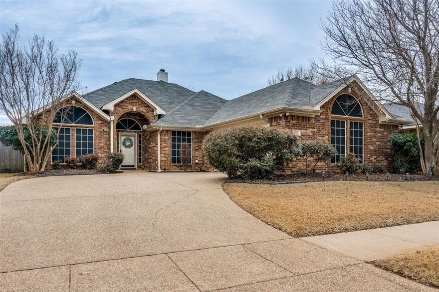 Located in desirable SW Arlington near US Hwy 287, this impeccably maintained full-brick home offers enduring craftsmanship in a small subdivision known for pride of ownership and low turnover. The J-swing garage and aggregate driveway create standout curb appeal and additional parking space for guests. Inside, rich custom built-in cabinetry in both the living area and dedicated office adds architectural character, abundant storage, and a refined, upscale feel rarely found at this price point. The family room centers around a handsome wood-burning fireplace framed in tile, detailed columns, and a substantial wood mantel—creating a warm, inviting focal point. The kitchen is both functional and beautifully appointed with built-in electric appliances, a sit-in bar top, walk-in pantry, travertine stone backsplash, and a dry bar featuring glass inlay cabinets for elegant display and entertaining. A wide, open pass-through with decorative shelving enhances the flow between spaces. Enjoy casual meals in the bright breakfast nook or host gatherings in the formal dining room. The split primary suite is a true retreat with bay windows and a spacious ensuite bath offering dual vanities, separate walk-in closets, a garden tub, and separate shower. A large, covered patio with soaring 10-foot ceilings overlooks the expansive, level backyard with mature grass and a large, custom brick patio—ideal for outdoor entertaining. Convenient to major employers, shopping, dining, and higher education, this is a rare opportunity to secure a meticulously cared-for home in an established, highly accessible location.