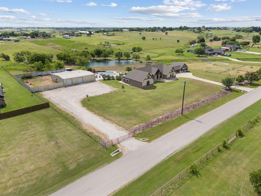 This stunning traditional, custom-built, one-story Texas estate perfectly blends classic charm with high-end luxury! Situated on 5.62 beautiful gated acres, outside city limits and close to the new Sanger High School- this timeless property with gorgeous main residence featuring an INDOOR BASKETBALL COURT, a large 3 bedroom, 1200 sf guest house and enormous 3600 sf shop that rivals any sports bar with video wall and fully equipped saloon- offers space, privacy and exceptional lifestyle features for both relaxation and entertaining! Upon entering the main residence, you will immediately fall in love! The gorgeous entryway welcomes you into the dining and formal living rooms while the open floor plan is ideal for entertaining in both the living room and chef's dream of a kitchen. Natural light pours in through the wall of windows in the front and back of the living areas flowing seamlessly into the backyard paradise! The spacious primary bedroom with spa-like primary bathroom and closet with custom built-ins, connecting to the laundry room for efficiency and ease- is separated from the 3 secondary bedrooms, each with large walk-in closets, full bath and a jack-n-jill bath, giving the utmost privacy. The entire home boasts beautiful flooring throughout and unique custom upgrades that elevate every room- from designer light fixtures, custom built-ins in the kitchen, laundry room, every walk-in closet and office to the beautifully crafted stone fireplace and everything in between! The luxury continues outside in your private paradise- a massive resort-style pool with slide, grotto and cascading waterfall and full outdoor kitchen including a smoker, pizza oven and grill are the perfect backdrop for spending your time enjoying the gorgeous Texas evenings overlooking the large stocked pond with several seating areas, a gorgeous waterwall feature, chipping mats and multiple fireplaces, you'll never want to leave! All of this plus LOW taxes with a wildlife exemption!