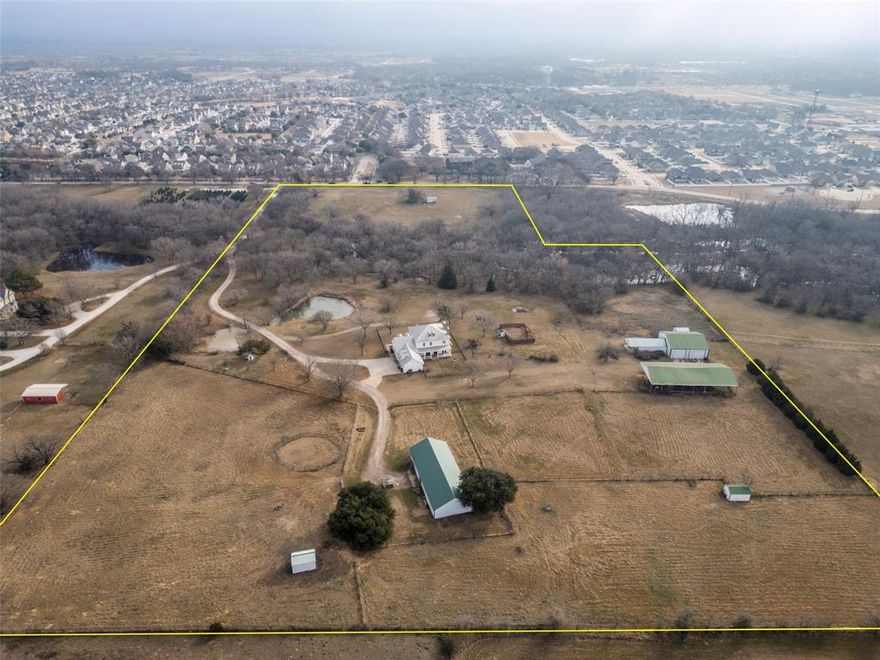 Stunning gated Southern Colonial estate set on 21.6± private acres in Denton County, nestled within the sought-after Prairie Acres community and ideally located between Little Elm, Providence Village, Cross Roads, and Aubrey. Set nearly one-eighth mile off the road, this impeccably maintained property offers exceptional privacy, timeless architecture, and refined rural living. Meticulously designed to reflect classic antebellum colonial styling, the home features three spacious bedrooms, a dedicated office or optional fourth bedroom, and three and a half baths. Three beautiful fireplaces anchor the thoughtfully designed interior, while sweeping views from every window, door, porch, and balcony bring the surrounding landscape indoors. The light-filled interior offers an inviting chef’s kitchen with breakfast area, sizable pantry, and dumbwaiter, along with two elegant living areas and a formal dining room ideal for entertaining. Generous storage, an expansive mudroom, and a well-appointed laundry room add everyday functionality. The home’s classic appeal is further enhanced by a standing-seam metal roof and fenced front and backyard spaces. The agricultural and wildlife exemption supports livestock, hay production, and abundant wildlife, with regular sightings of whitetail deer and waterfowl drawn to the stocked pond and seasonal creek. Native pecan, oak, and elm trees create a picturesque, park-like setting. Equestrian and hobby amenities include an impressive eight-stall barn with tack room, stocks, and ample storage, four loafing sheds, a chicken house, and designated garden area. Additional improvements include a 50’ x 50’ shop and a 40’ x 25’ workshop. The property is fully fenced and cross-fenced for versatility and ease of use. A rare opportunity offering peaceful country privacy with convenient access to city amenities — truly an exceptional estate for those seeking elegance, functionality, and space to live fully.